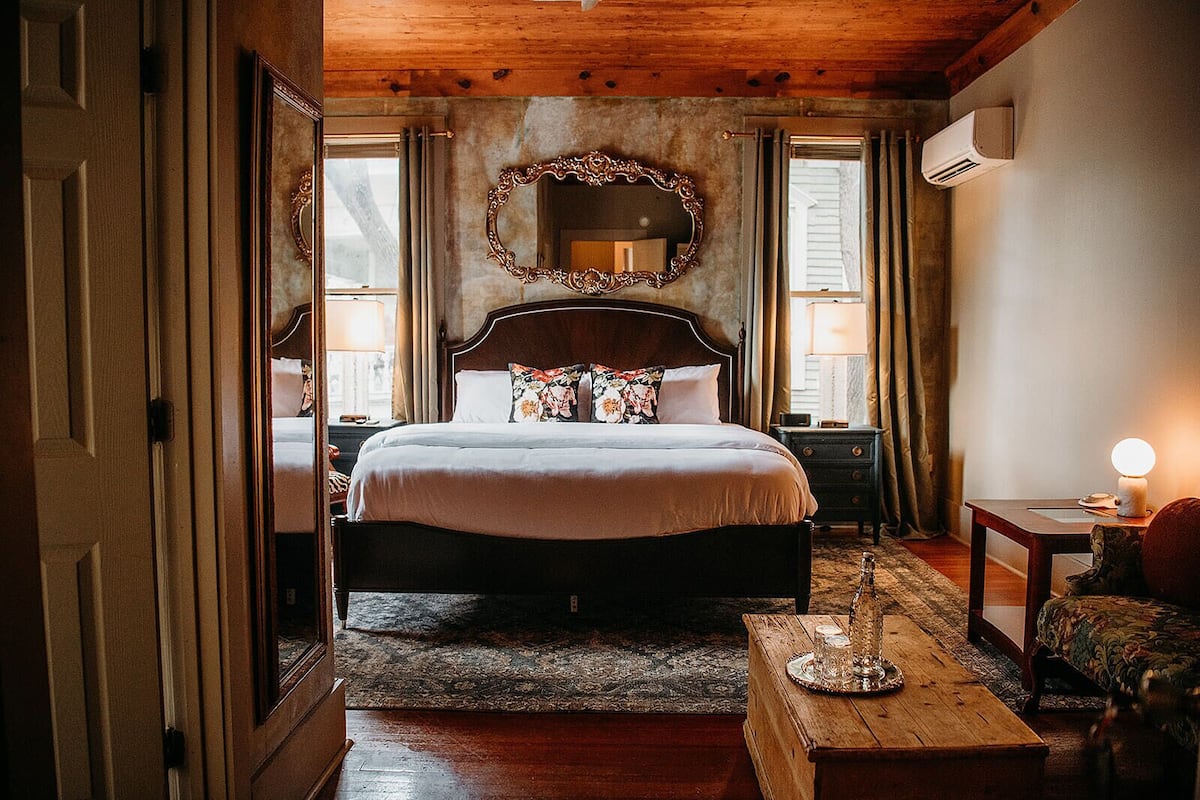 Une chambre à coucher avec un grand lit, un plafond en bois, un miroir et une table de chevet avec une lampe.