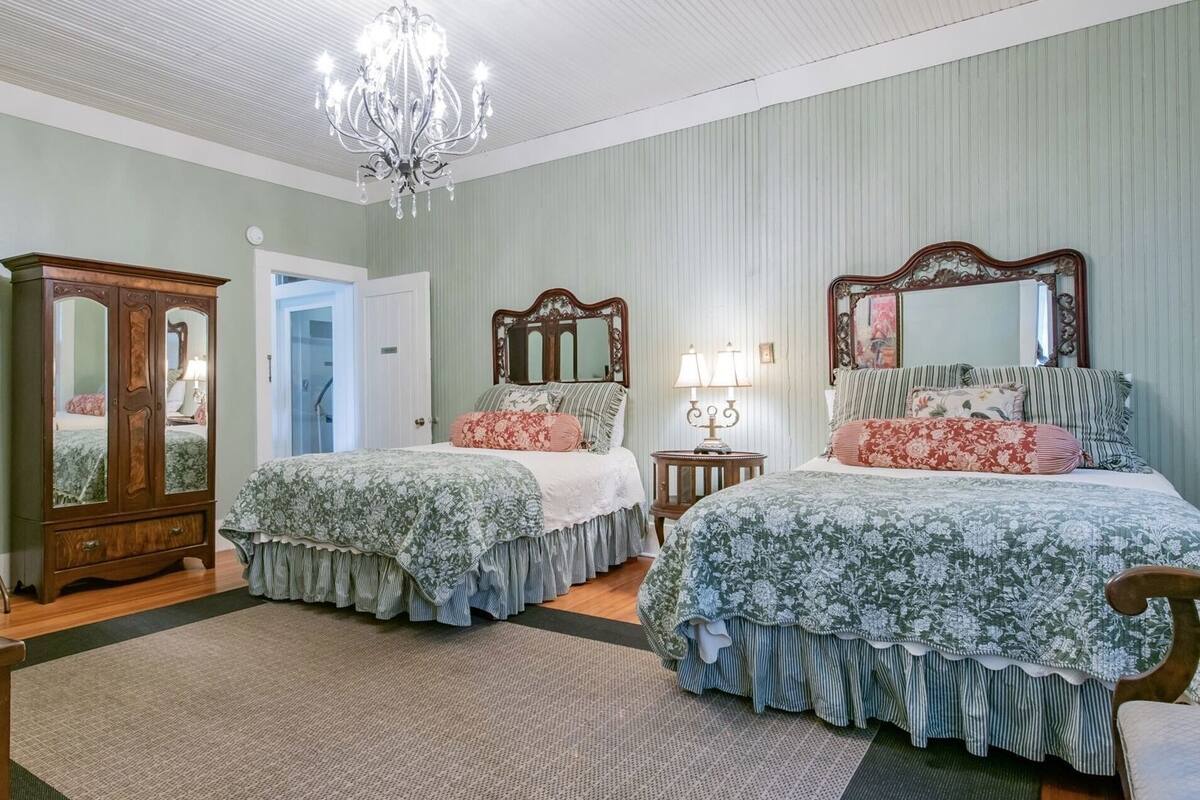 Une chambre à coucher avec deux lits, un lustre, une armoire et un miroir.