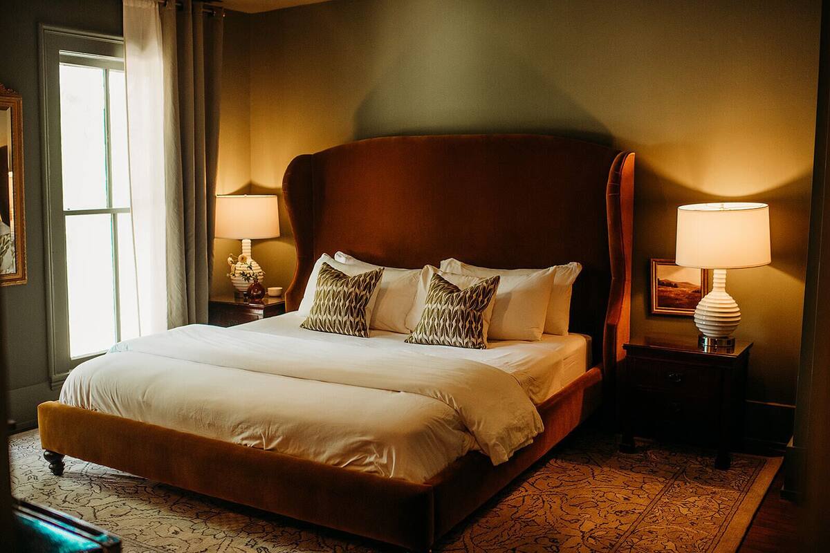Un grand lit avec une tête de lit en bois, deux tables de chevet avec des lampes et un tapis à motifs.