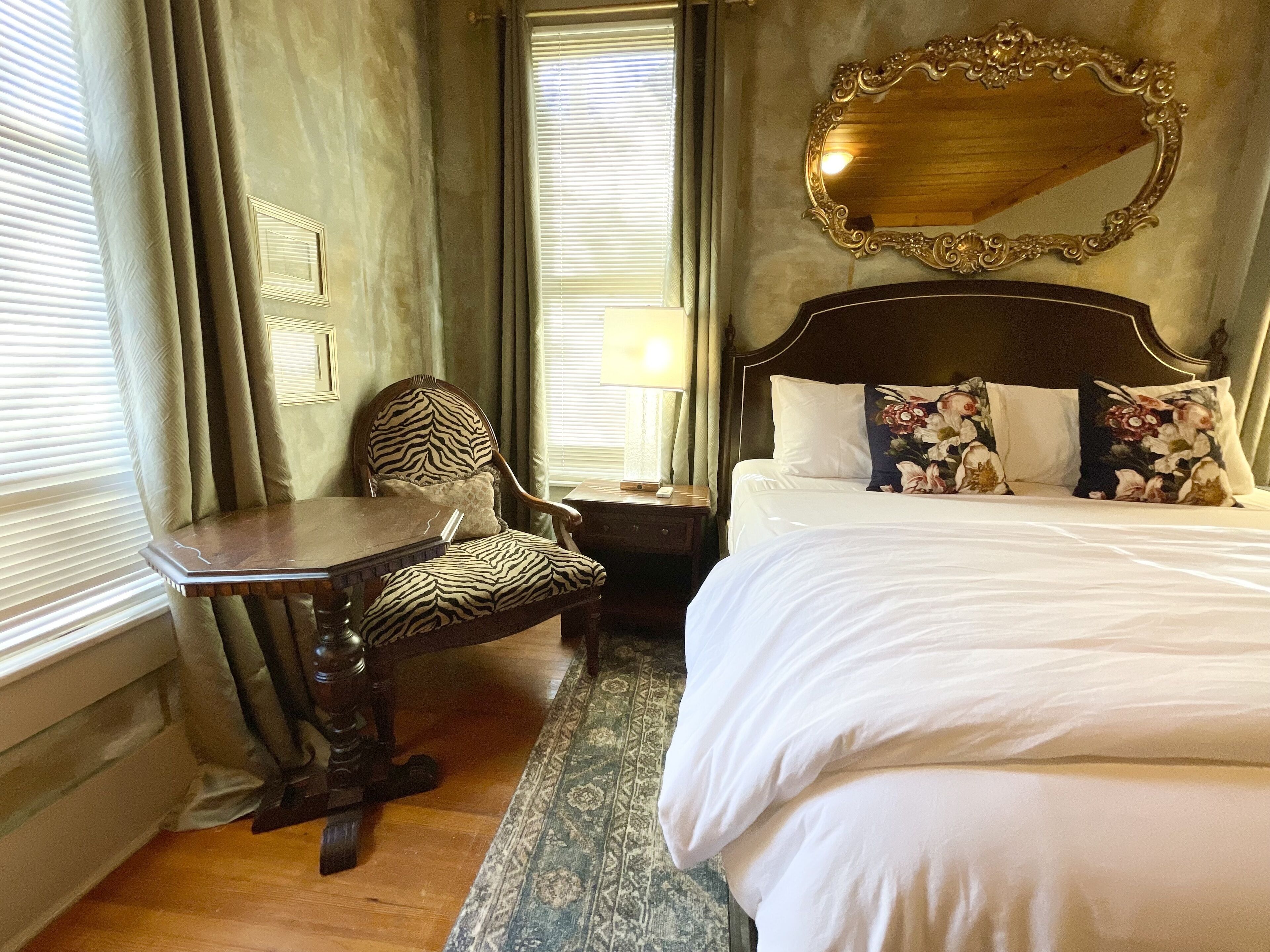 A hotel room with a bed, a chair, a desk, and a large mirror.