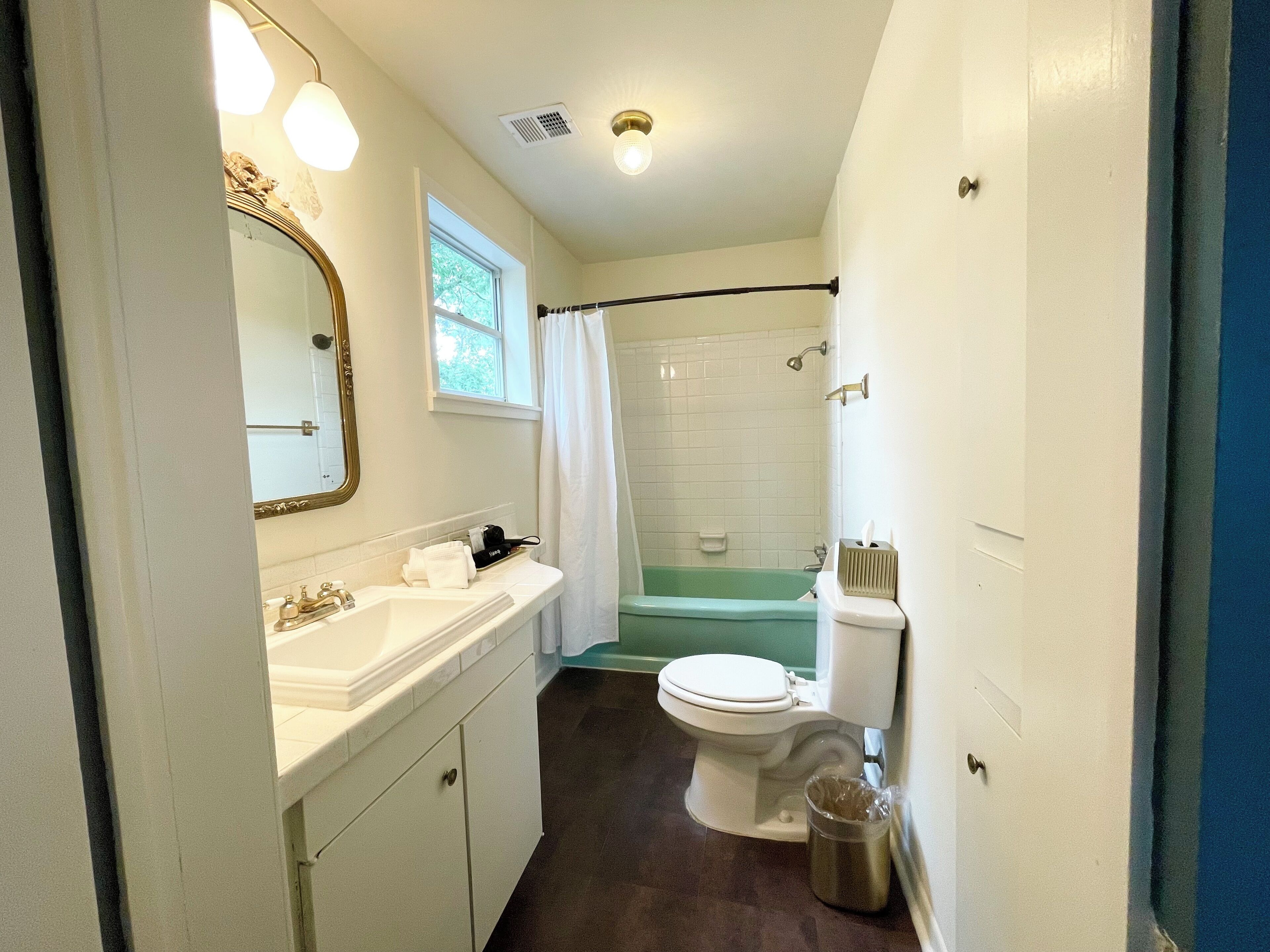 A compact bathroom with a white sink, vanity, and toilet. A bathtub is visible in the background, and a shower curtain is hanging.