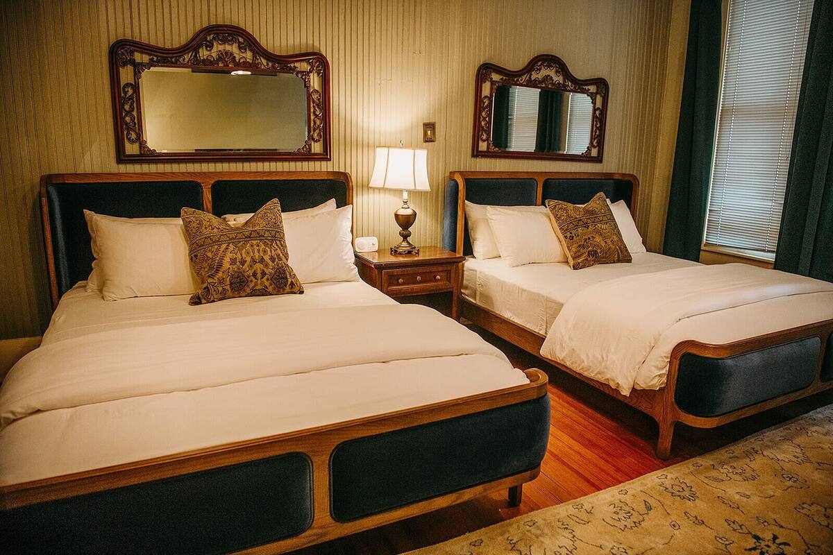 Une chambre d’hôtel avec deux lits doubles, une table de chevet avec une lampe et deux miroirs fixés au mur.