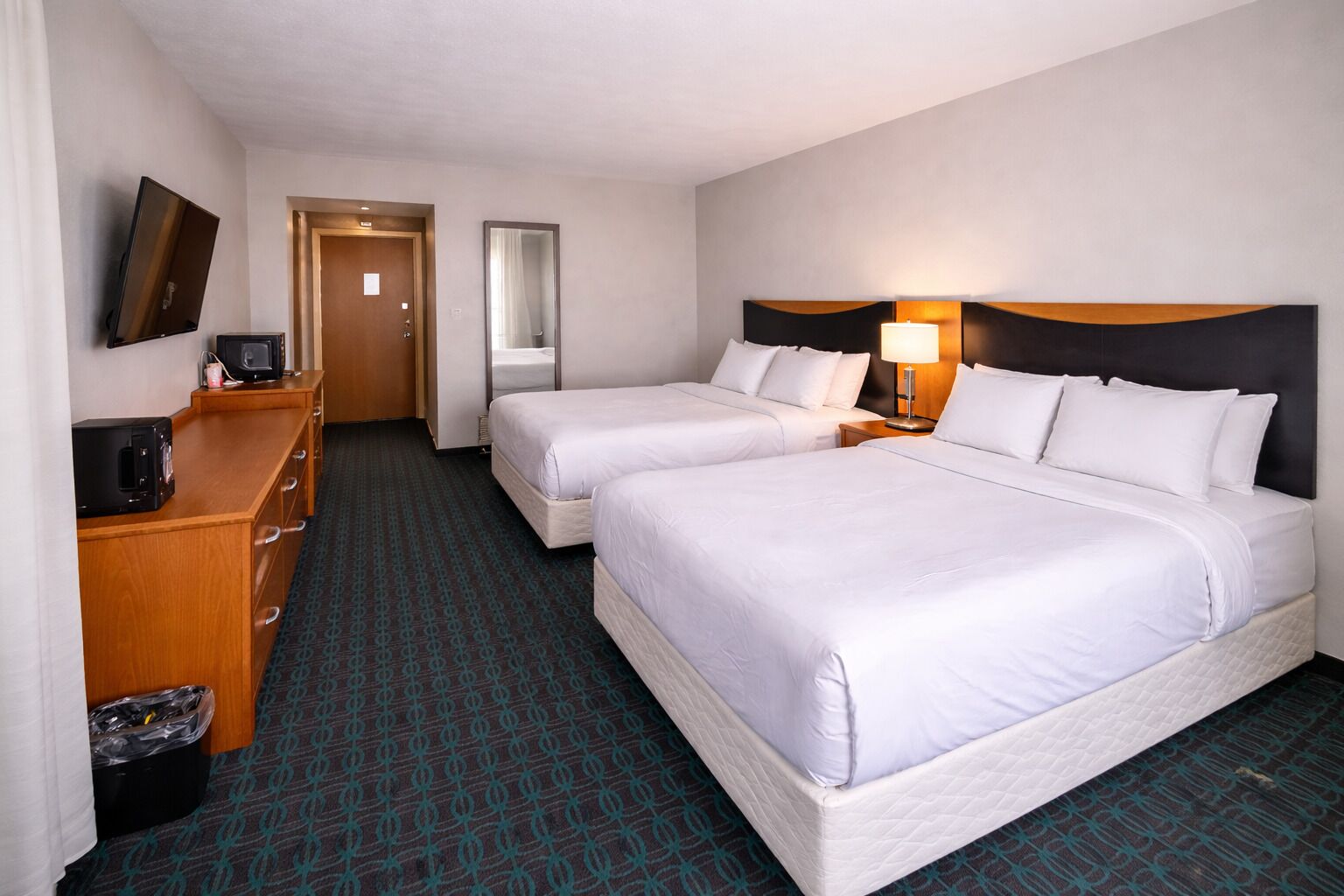 A hotel room with two beds, a TV, a desk, and a mirror.