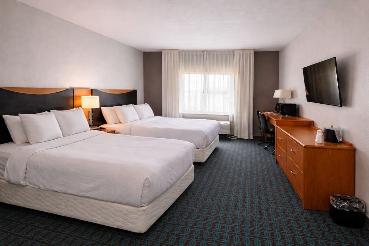 Habitación de hotel con dos camas, un escritorio, un televisor y una ventana con cortinas.