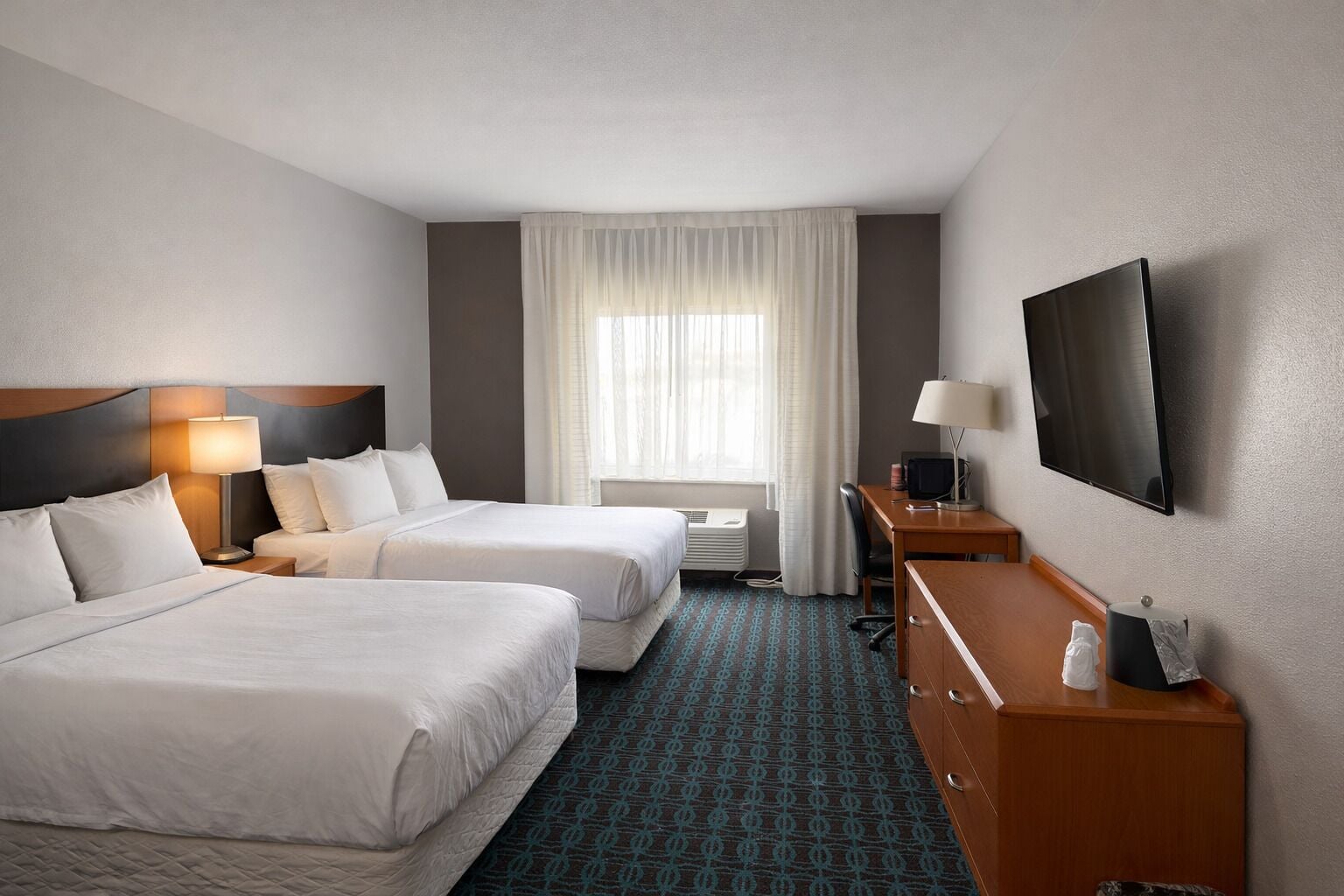 Una habitación de hotel con dos camas, un escritorio, un televisor y un ventanal con cortinas.