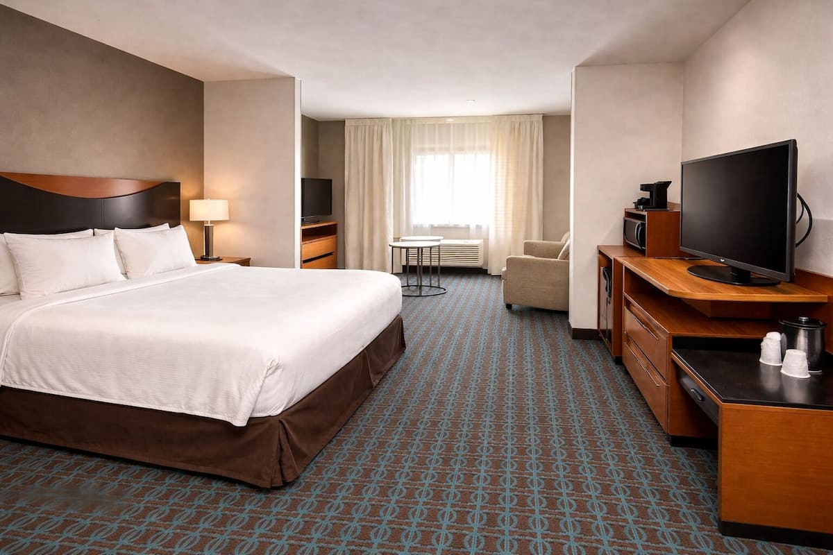 Habitación de hotel con una cama grande, televisión, escritorio con cafetera, una silla y una mesita.