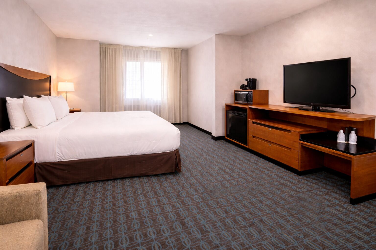 A hotel room with a bed, a desk with a television, a coffee maker, and a microwave.