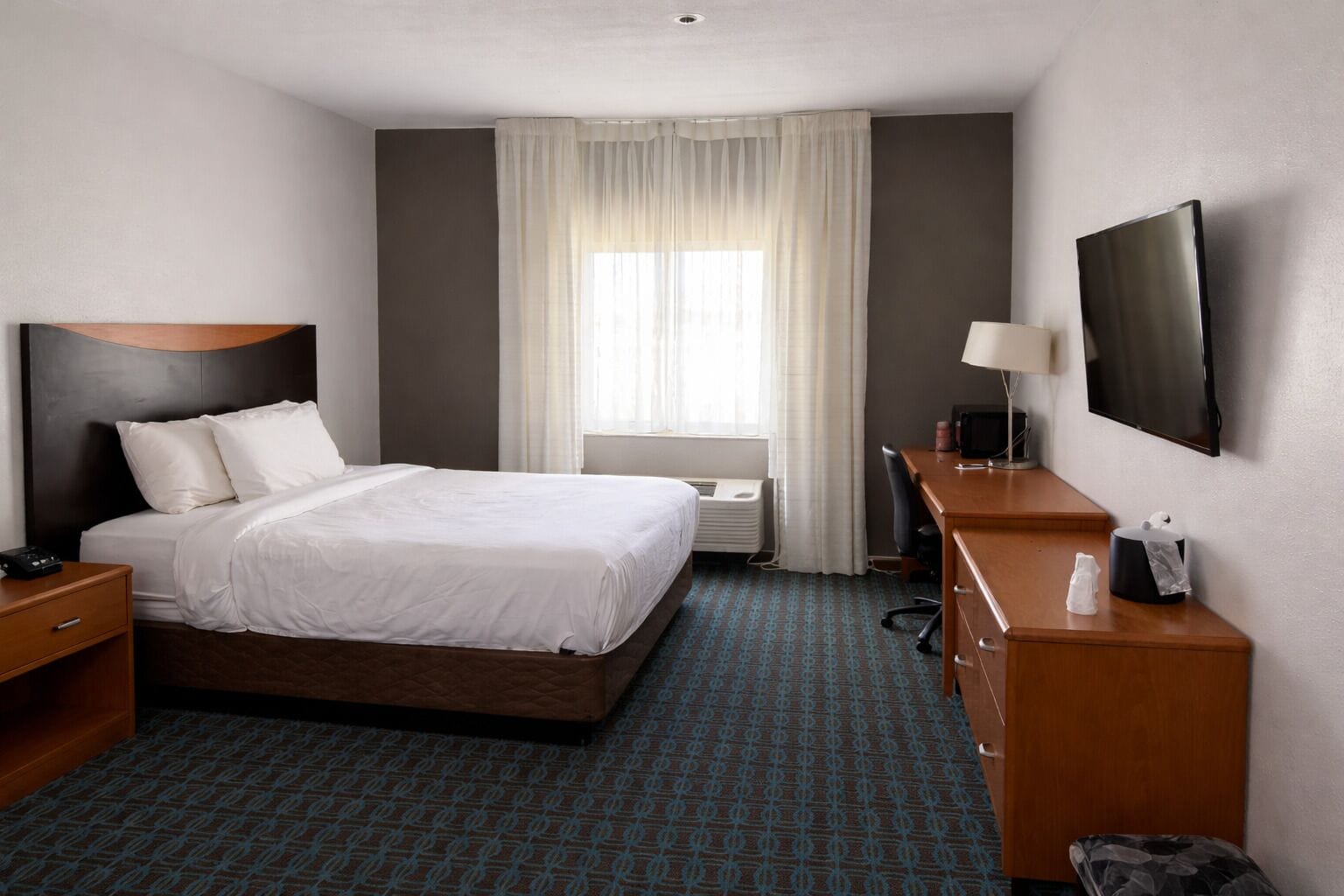 A hotel room with a bed, a desk, a TV, and a window with curtains.