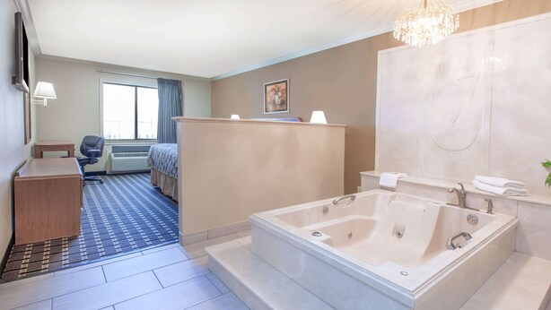 A hotel room with a large bathtub, a desk, a chair, and a bed. - Super 8 by Wyndham Tyler TX (Tyler)