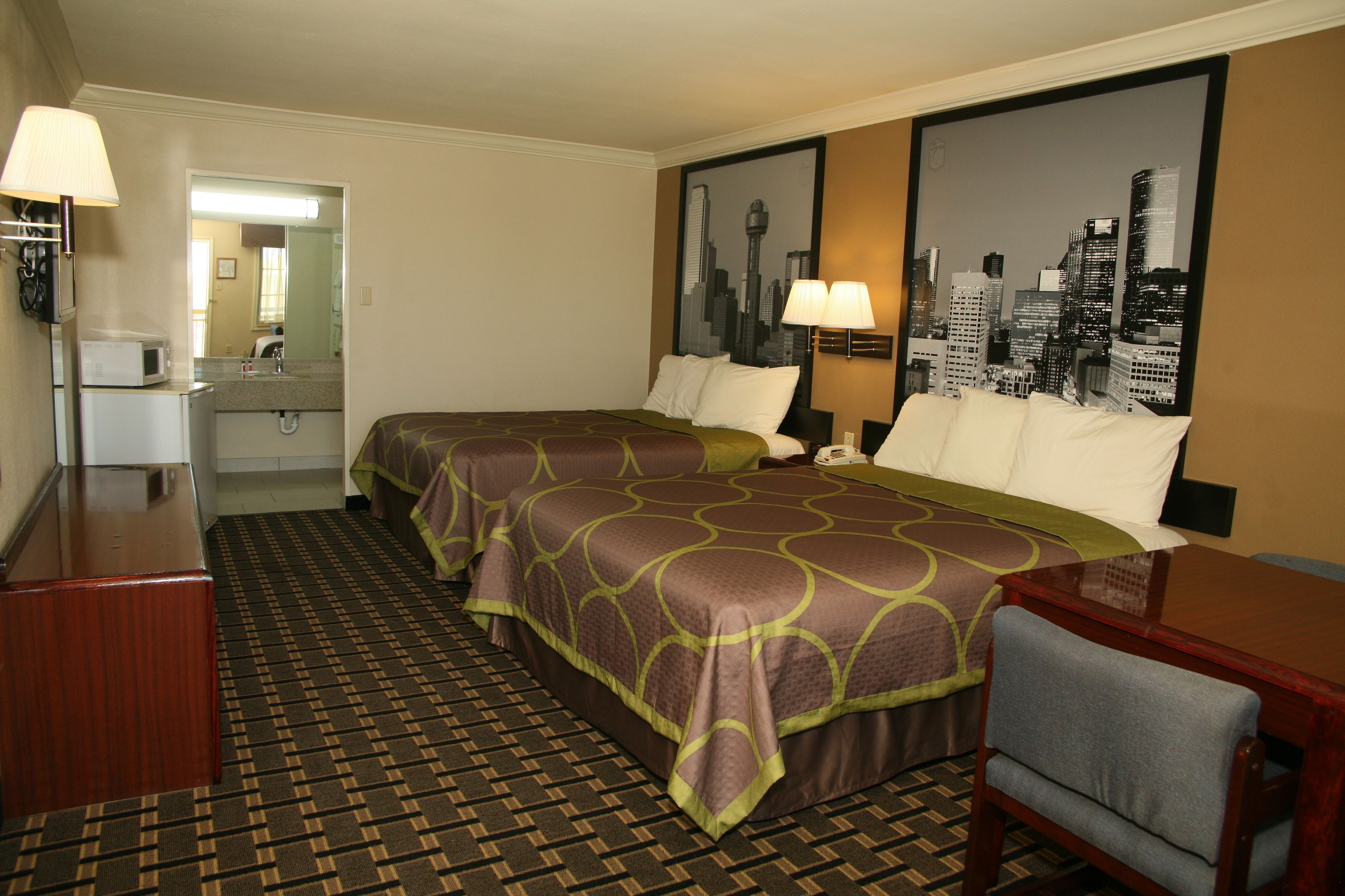 Een hotelkamer met twee bedden, een bureau, een stoel, een magnetron en een groot stadsgezichtschilderij aan de muur.