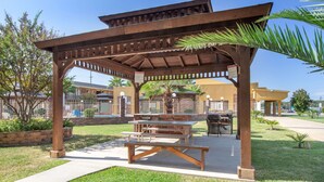 A covered picnic area with benches and a barbecue grill, surrounded by grass and palm trees. - Super 8 by Wyndham Tyler TX (Tyler)