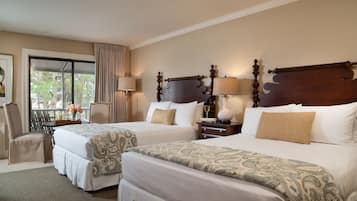 A hotel room with two beds, a sitting area with a chair, a table with a vase of flowers, and a view of trees through a window.
