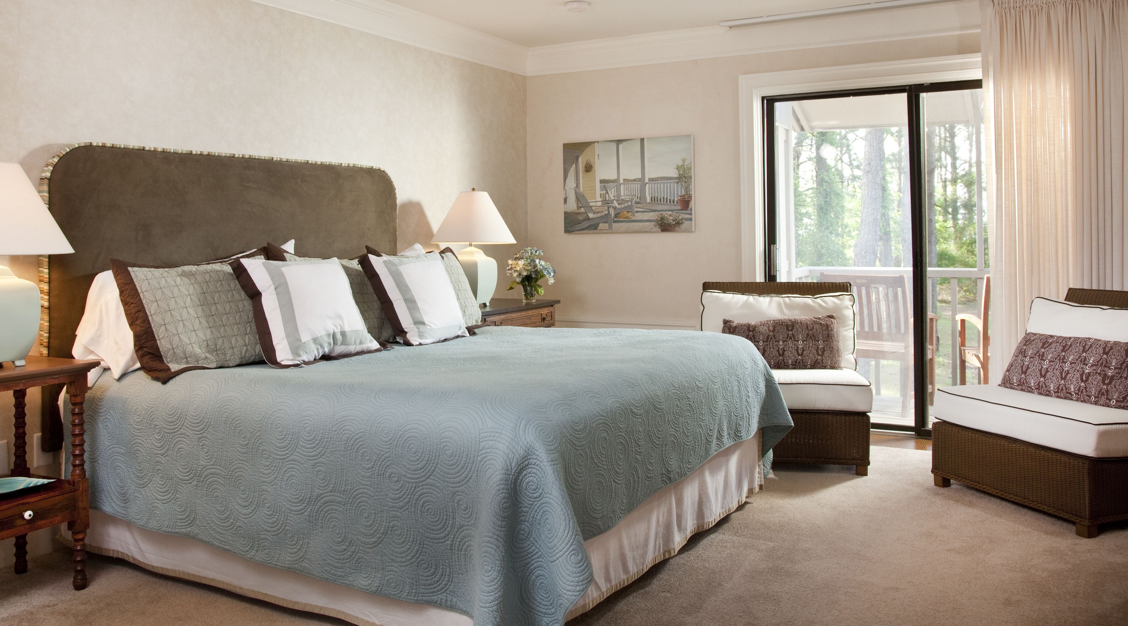 A bedroom with a large bed, a nightstand, a chair, and a window with curtains.