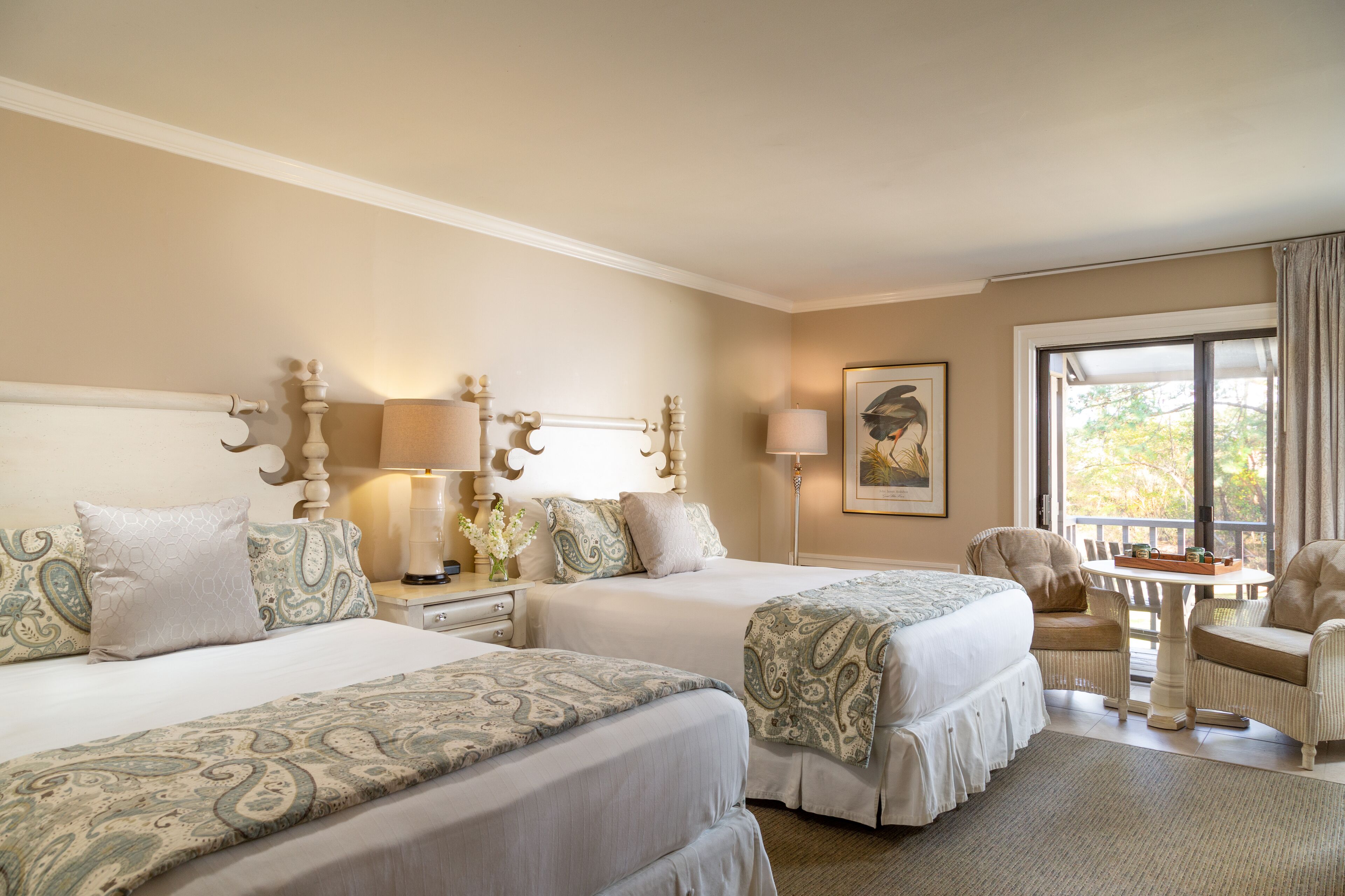 A hotel room with two beds, a sitting area with a table and chairs, and a large window with curtains.
