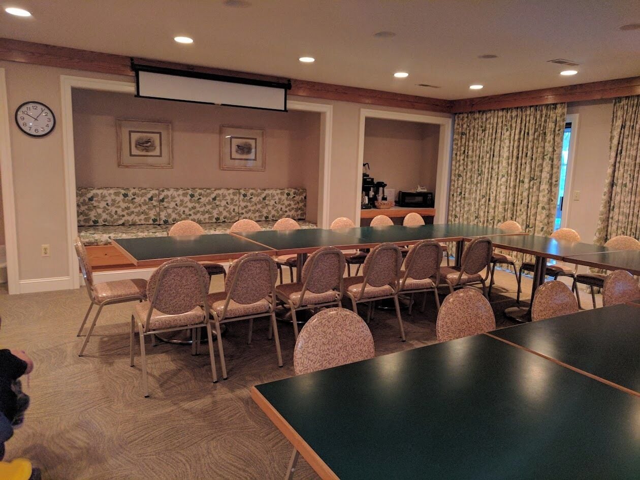A conference room with a long table and chairs, a clock on the wall, and a projector screen.