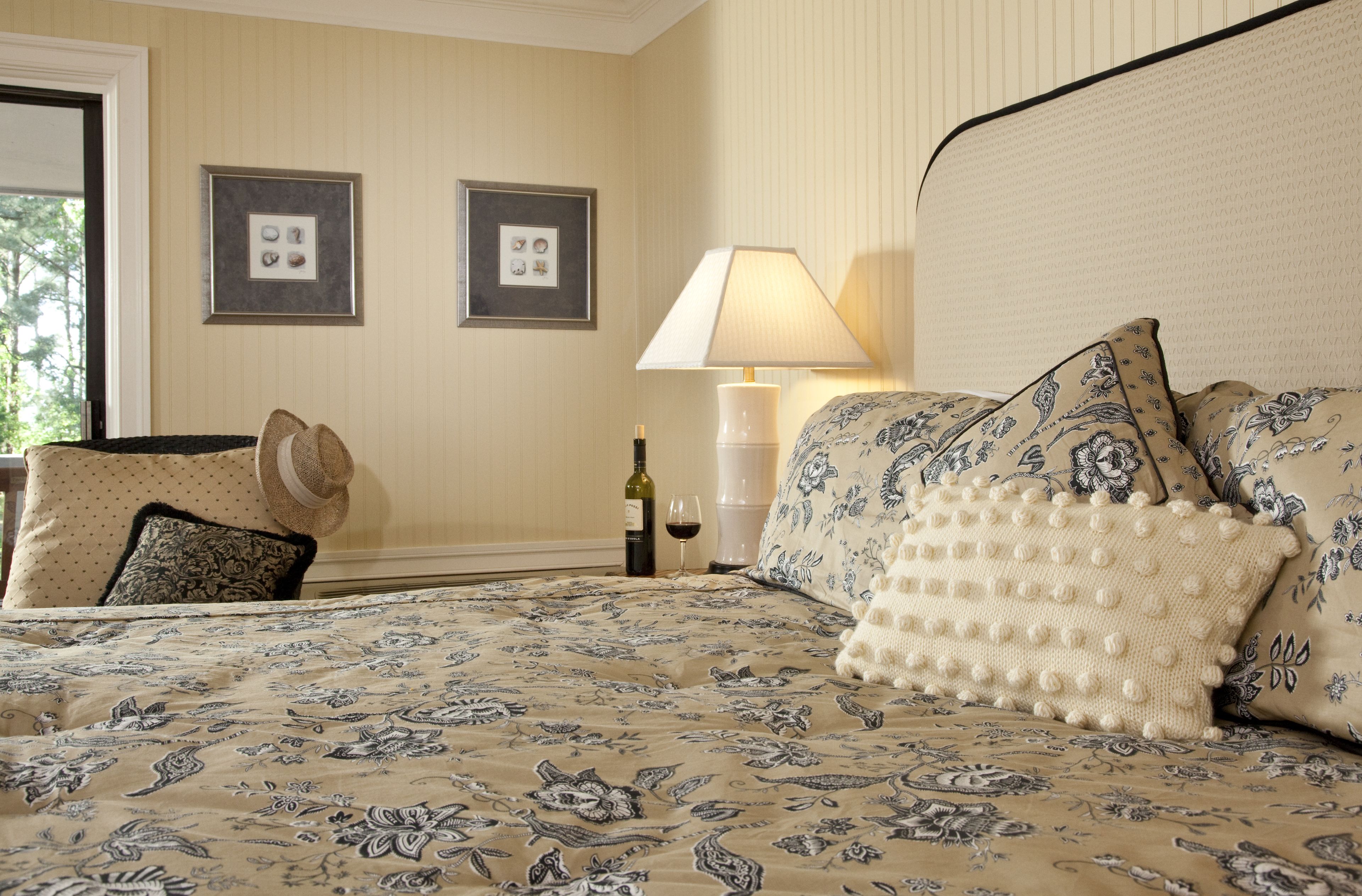 Une chambre à coucher bien rangée, avec une couvre-lit à motifs floraux, une lampe de chevet et un tableau encadré au mur.