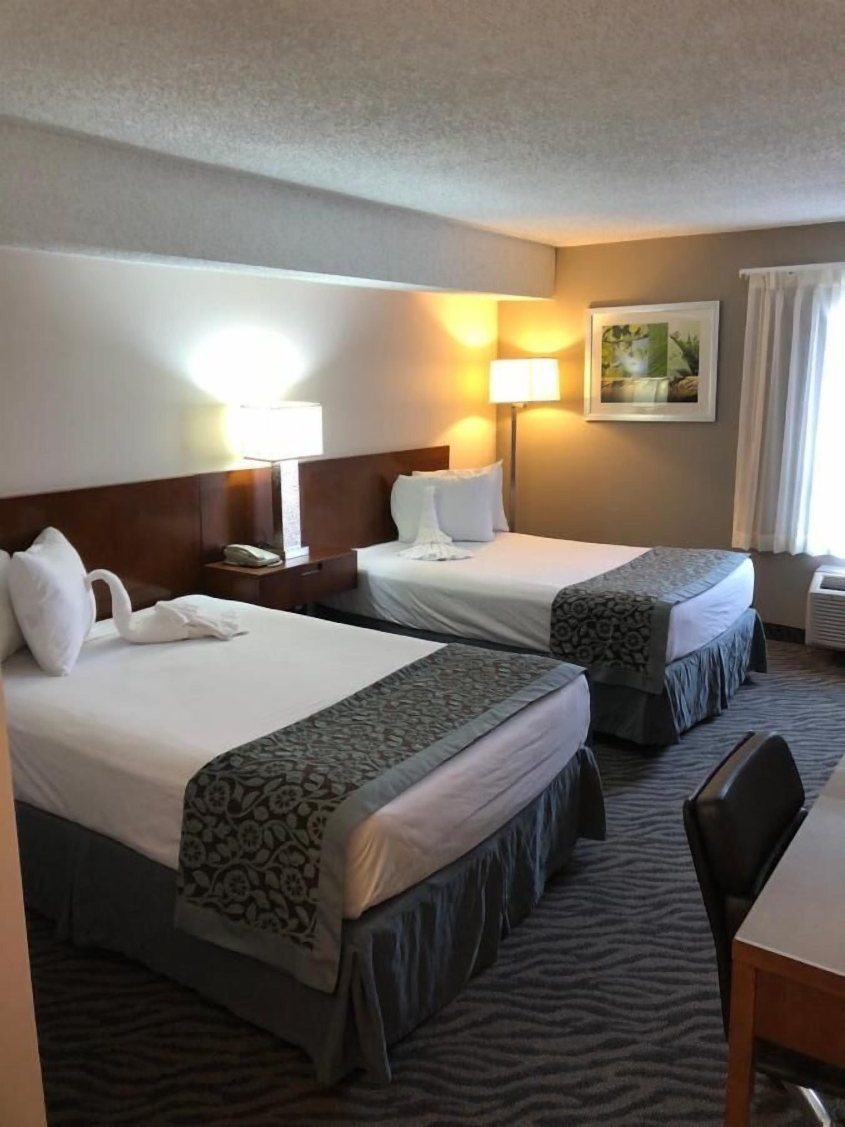 A hotel room with two beds, a desk, a chair, a lamp, and a picture on the wall.