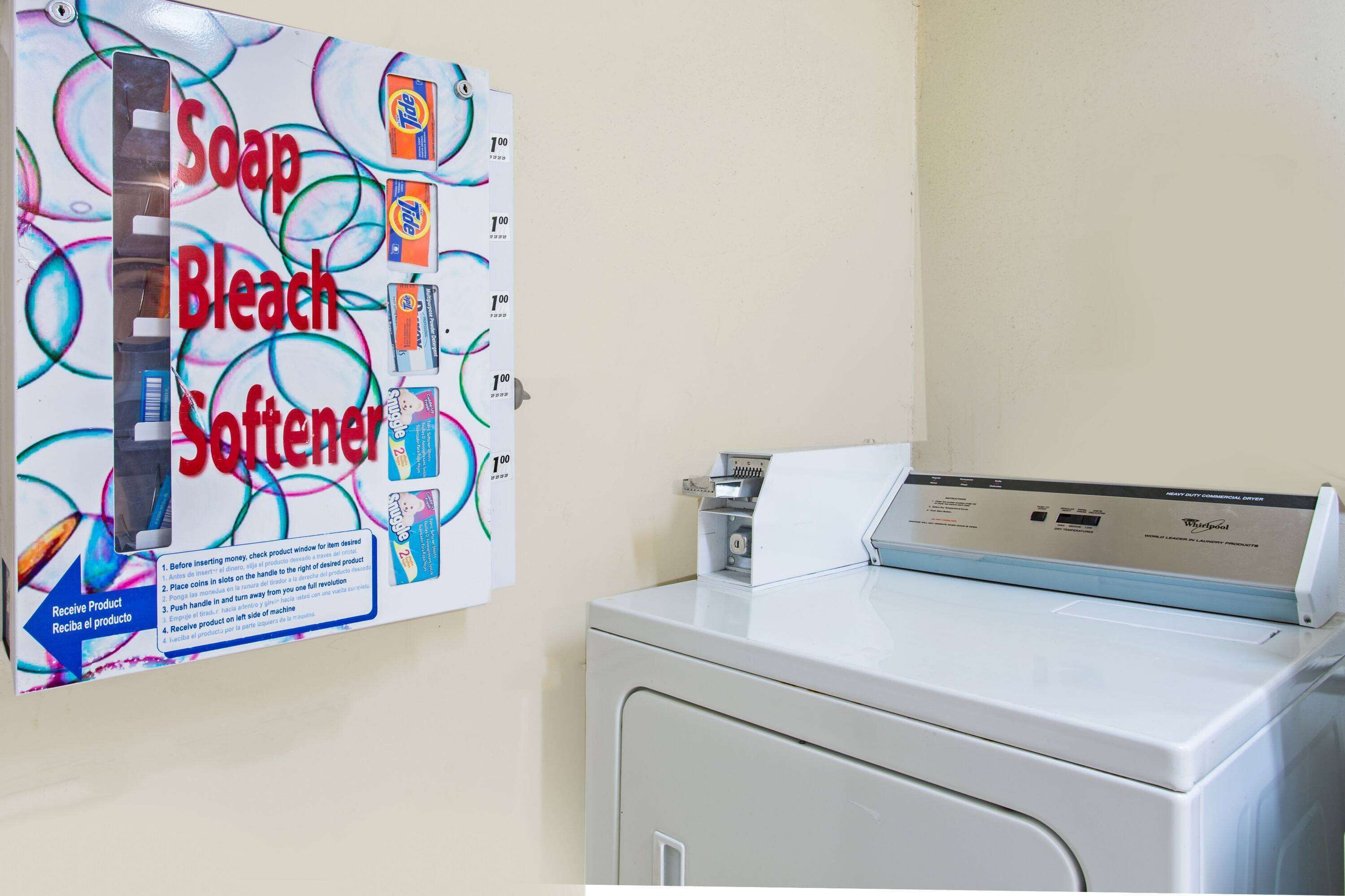 A laundry machine with a detergent dispenser and a wall-mounted soap, bleach, and softener dispenser.