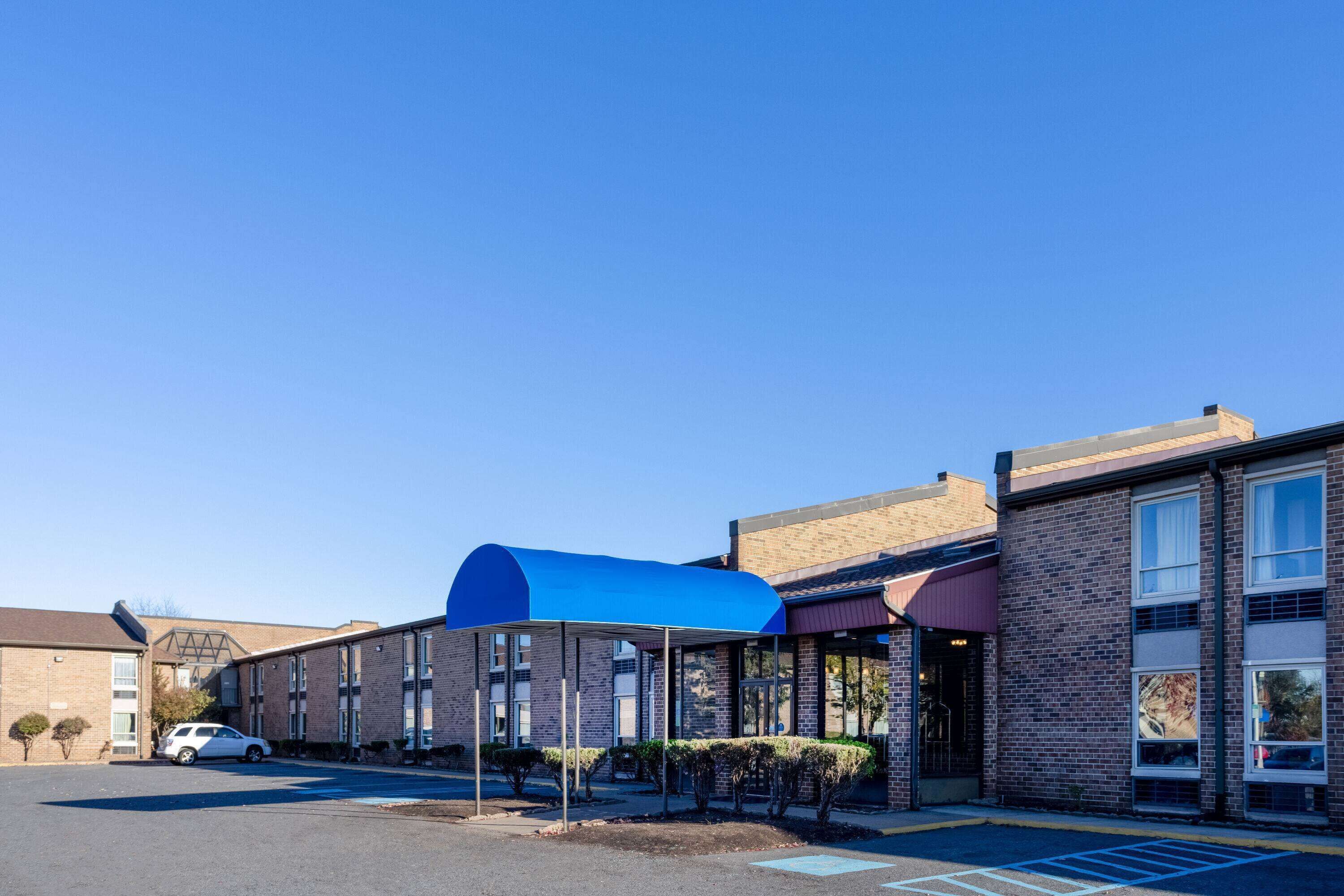 A hotel with a covered outdoor area, a parking lot, and a brick building facade.