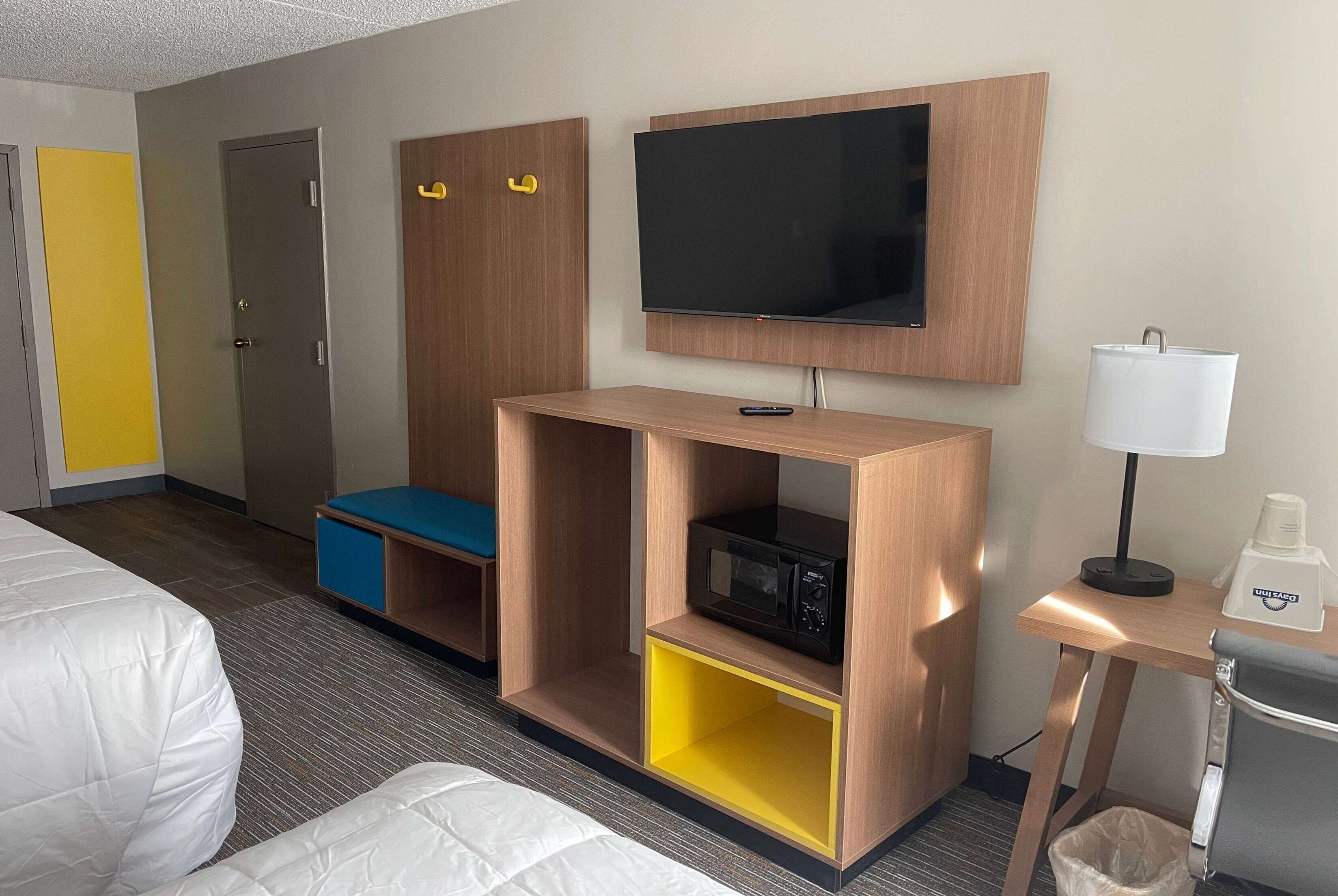 A hotel room with a bed, a TV, a microwave, a lamp, and a small table with a coffee maker.