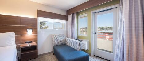 A hotel room with a bed, a small desk, a chair, a window, and a door.