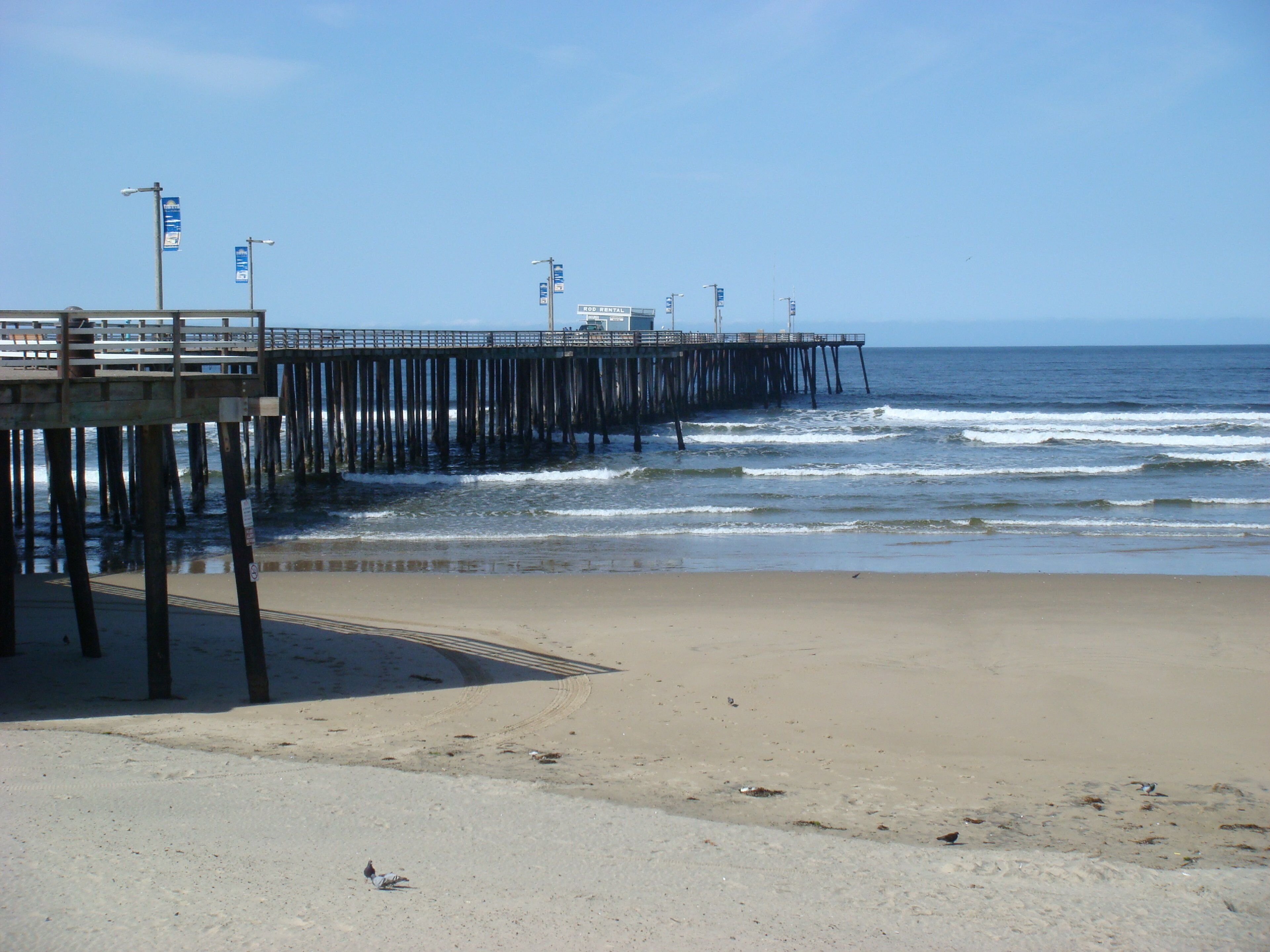 A pier extending into the ocean with a sandy beach in the foreground.