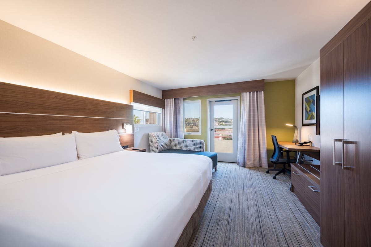 A hotel room with a large bed, a desk, and a view of the outdoors.