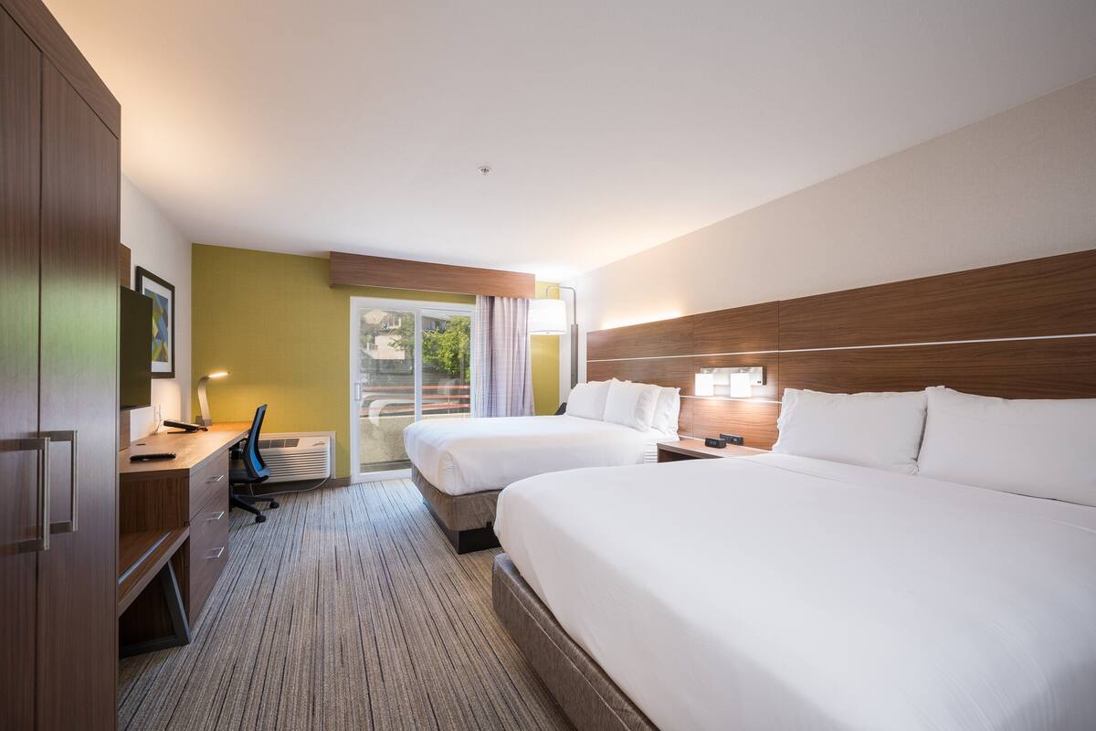 A hotel room with two beds, a desk, a chair, and a window with a view.