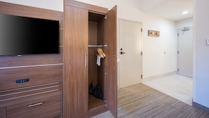 A hotel room with a wooden wardrobe, a flat-screen TV, a door with a towel rack, and a shower area.
