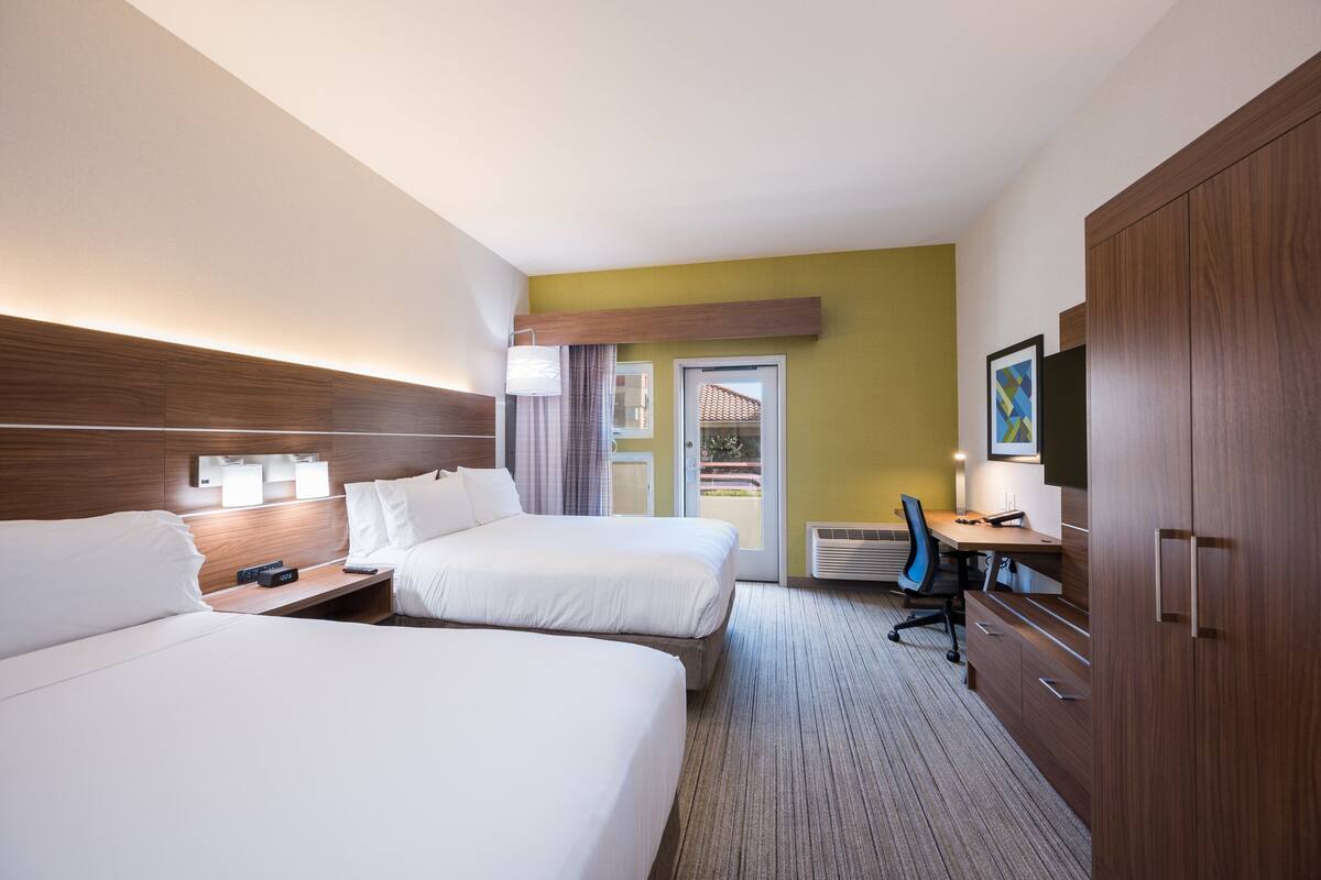 A hotel room with two beds, a desk, a chair, a TV, and a wardrobe.