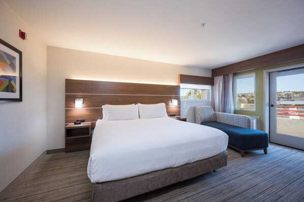 Una camera d'hotel moderna con un letto grande, un comodino, una sedia e vista sull'esterno.
