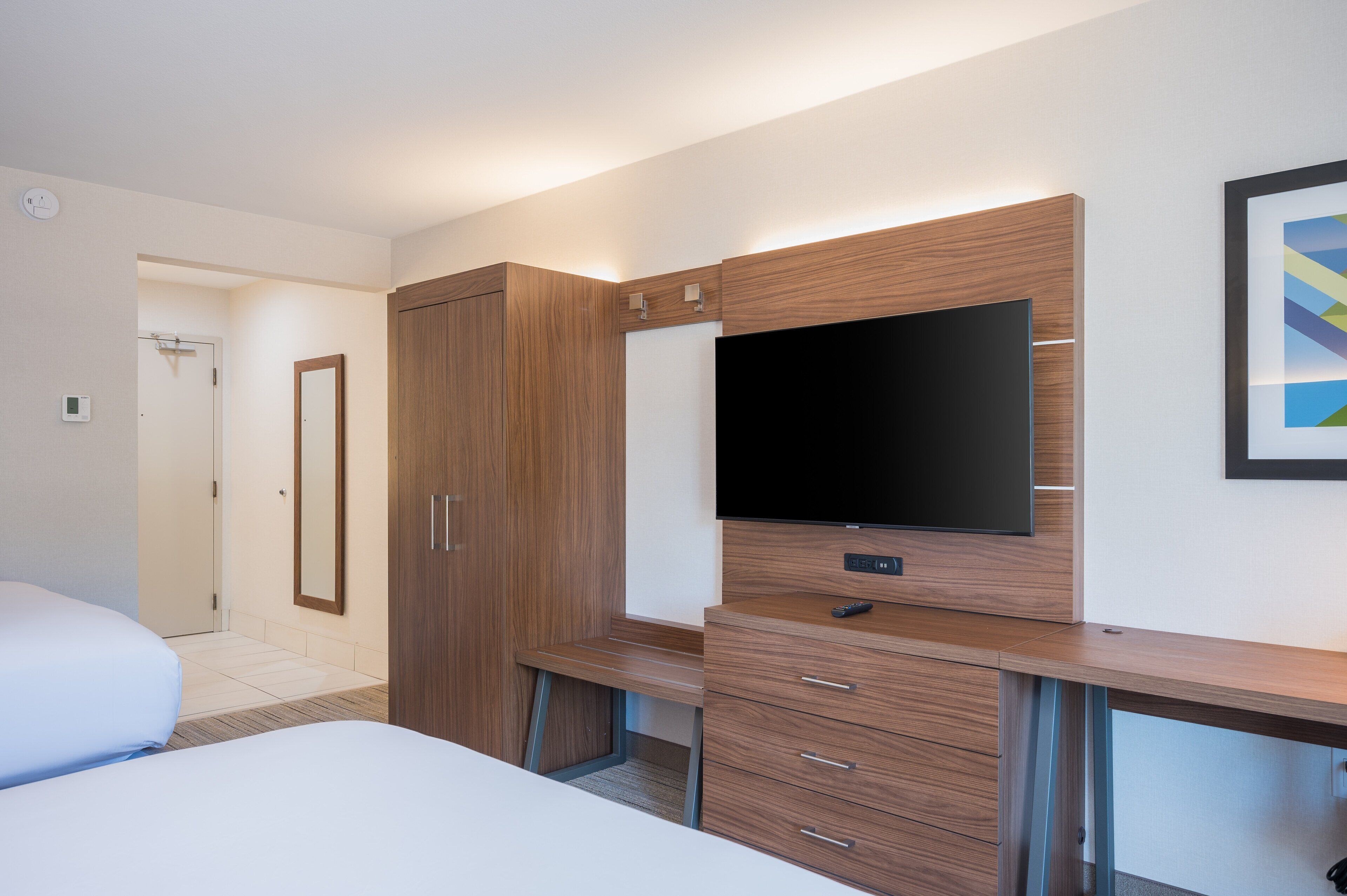 A hotel room with a bed, a desk with drawers, a television, and a mirror.
