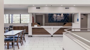 A modern hotel lobby with a reception desk, seating area, and large windows.