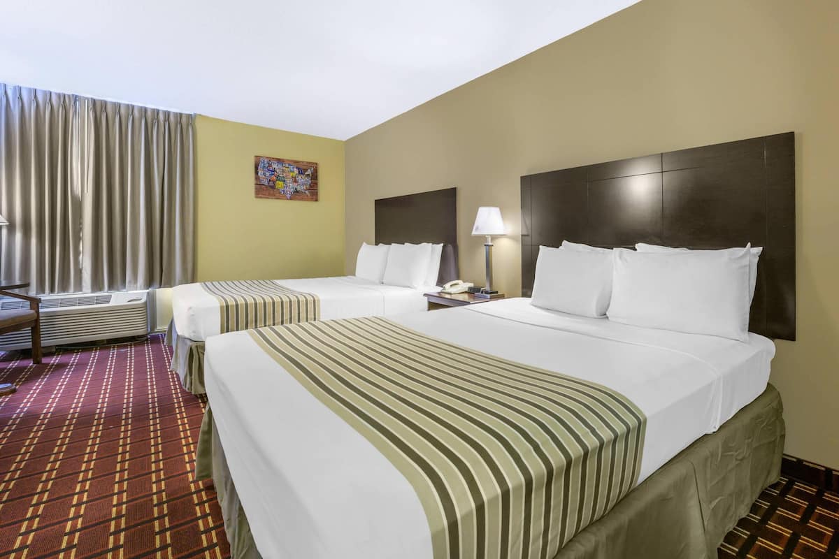 A hotel room with two beds, a large window with curtains, a wall-mounted lamp, and a patterned carpet.