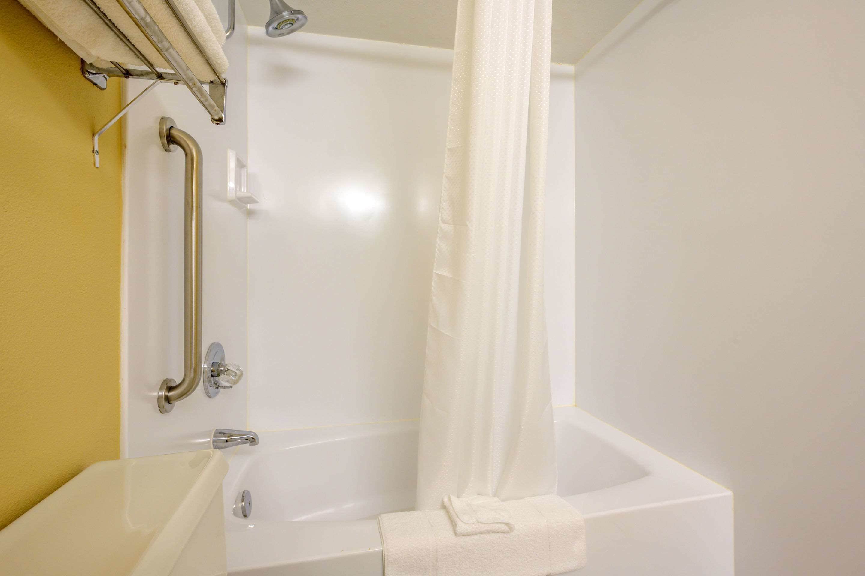 A bathroom with a bathtub, a shower curtain, a towel, and a grab bar.