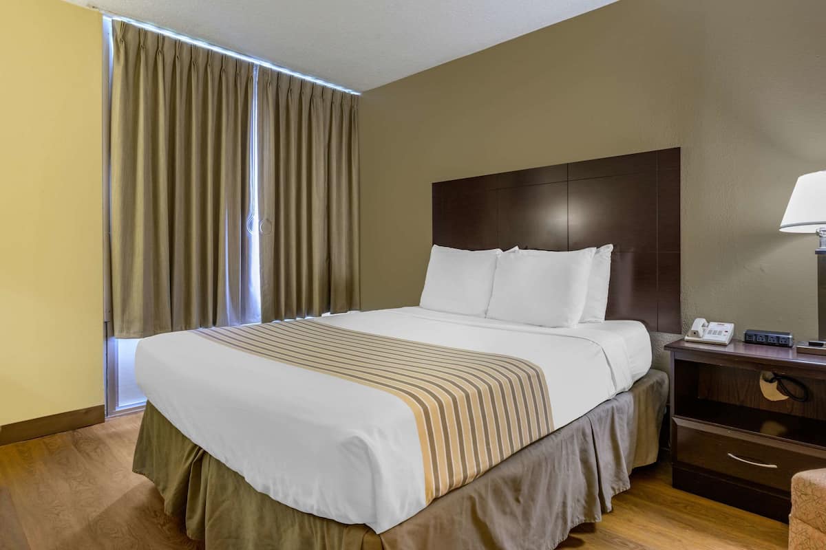 A hotel room with a large bed, a nightstand with a lamp, and a window with curtains.