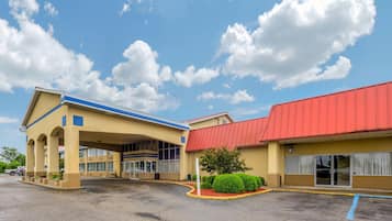 A hotel with a covered entrance, a red roof, and a parking lot.