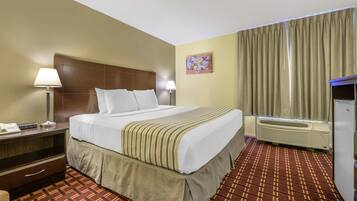 A hotel room with a bed, nightstand, lamp, air conditioning unit, and a patterned carpet.