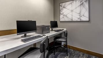A hotel room with a desk, two monitors, a keyboard, a mouse, and a chair.