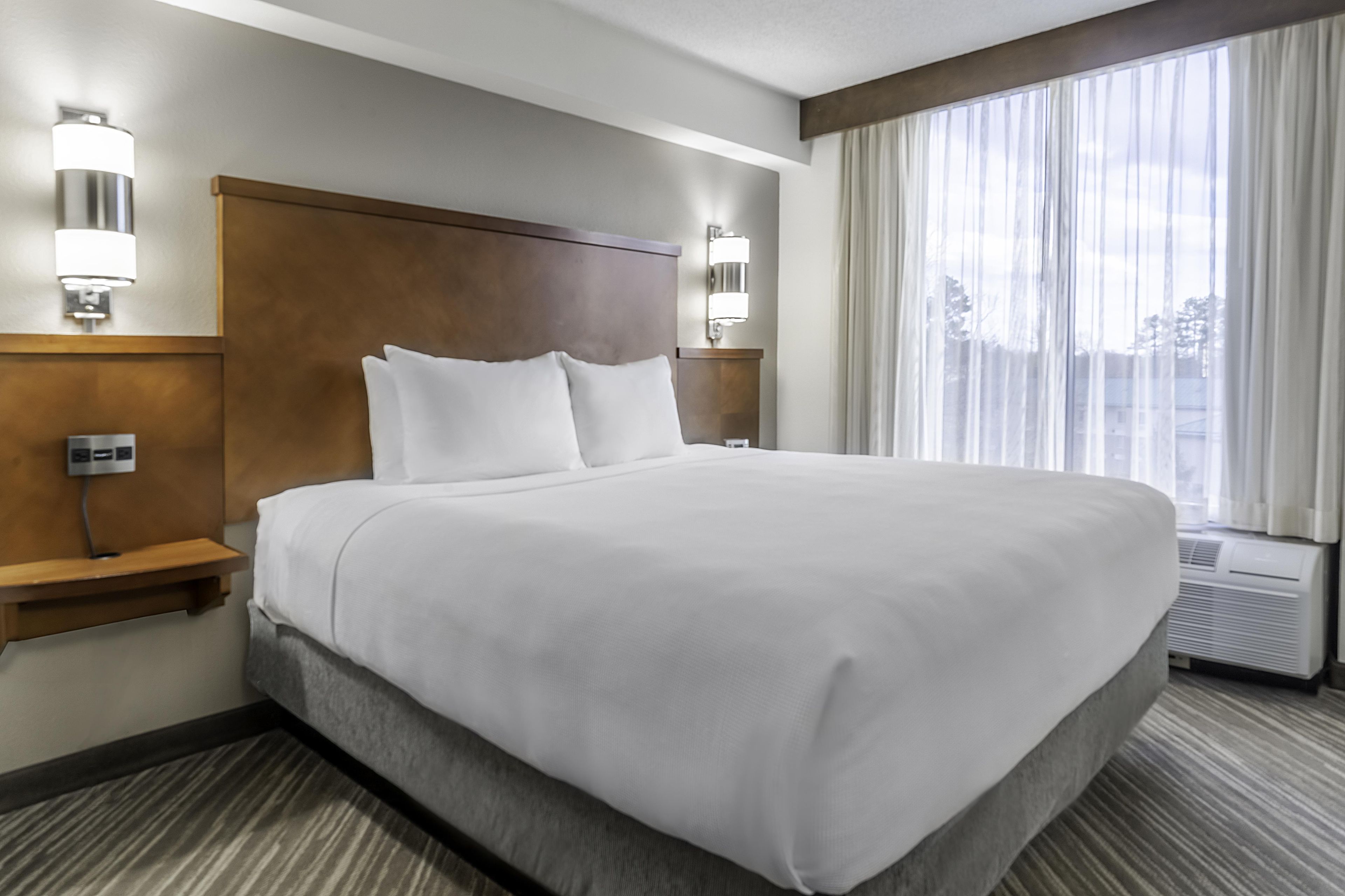 Ein Hotelzimmer mit einem großen Bett, zwei Nachttischen, einem Kopfteil und einem Fenster mit Vorhängen.