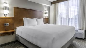 Ein Hotelzimmer mit einem großen Bett, zwei Nachttischen, einem Kopfteil und einem Fenster mit Vorhängen.