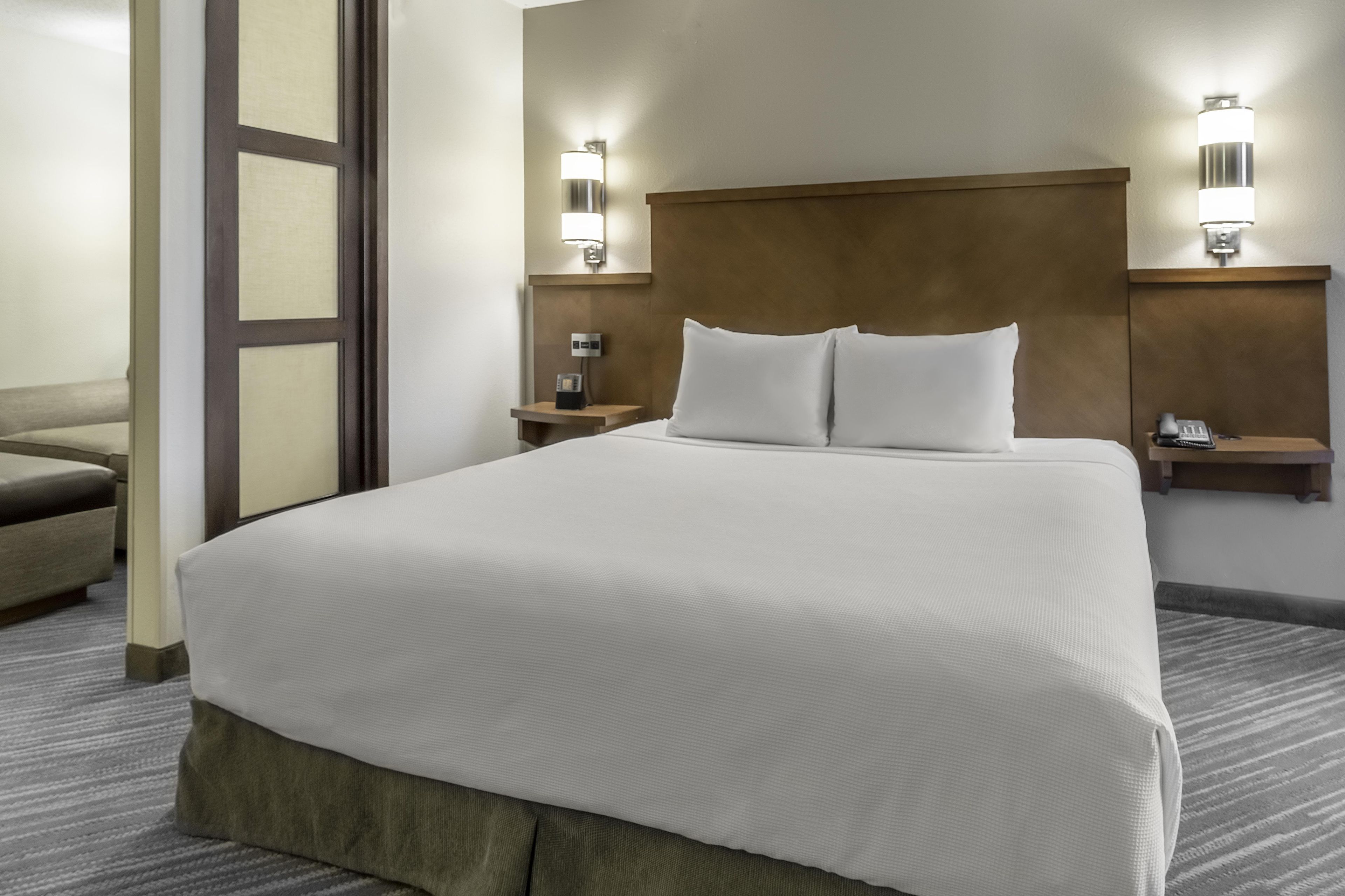 Une chambre d’hôtel avec un grand lit, deux tables de chevet, une chaise et un téléphone fixé au mur.