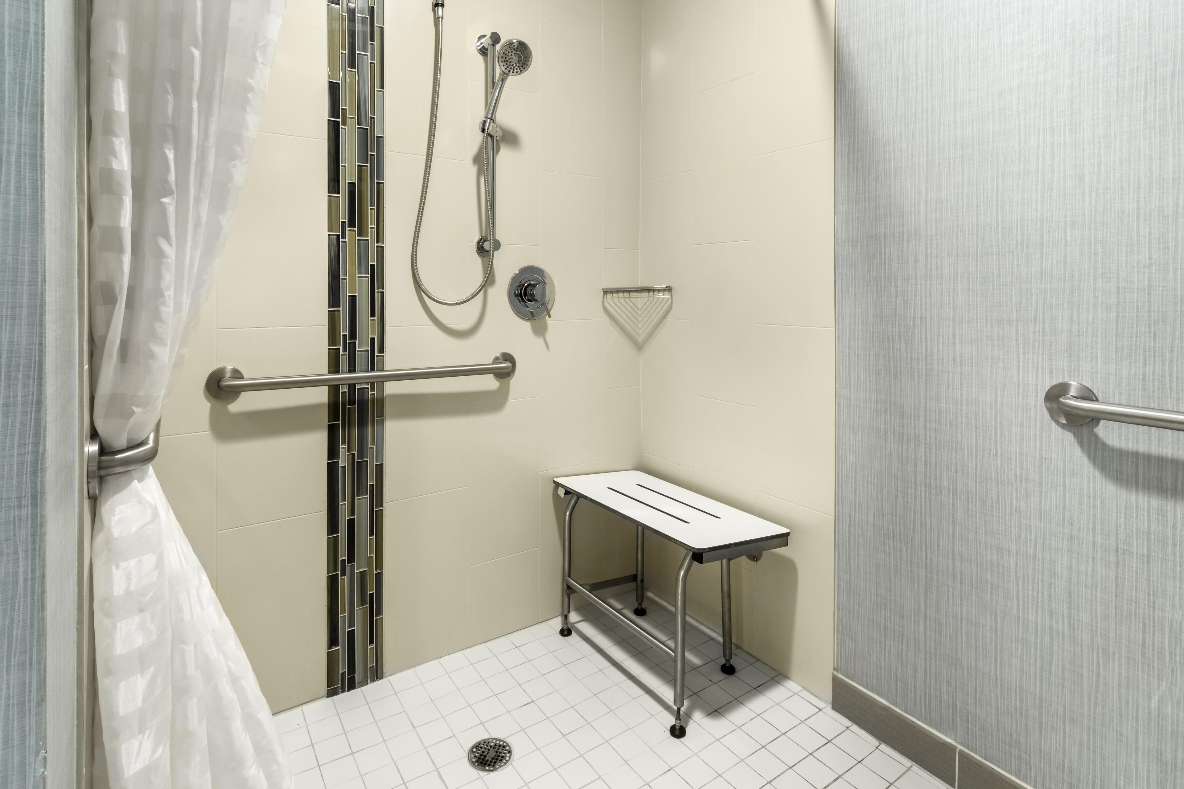 A small, enclosed shower area with a grab bar, a showerhead, and a floor drain.
