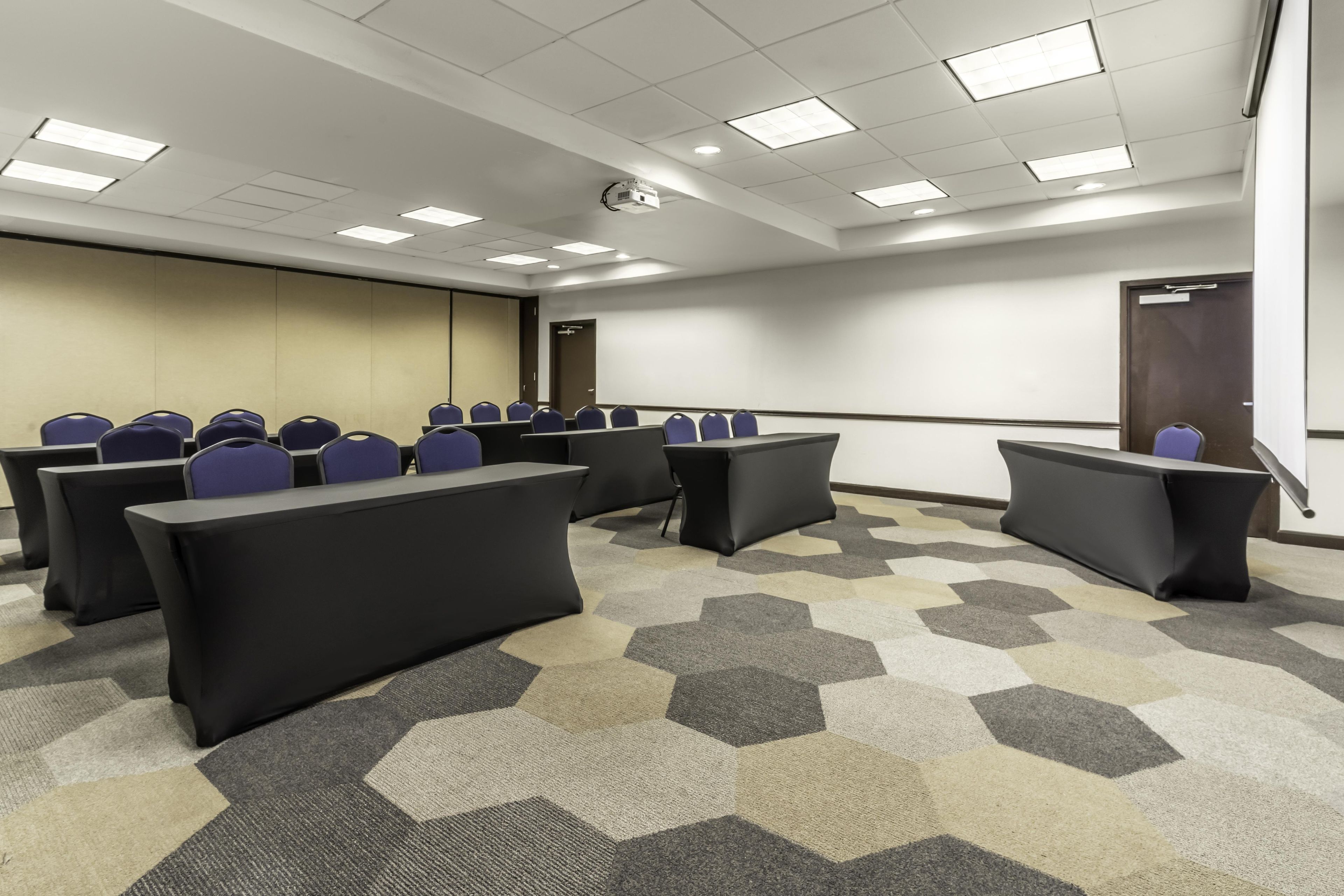 A conference room with tables and chairs, a projector, and a carpeted floor.