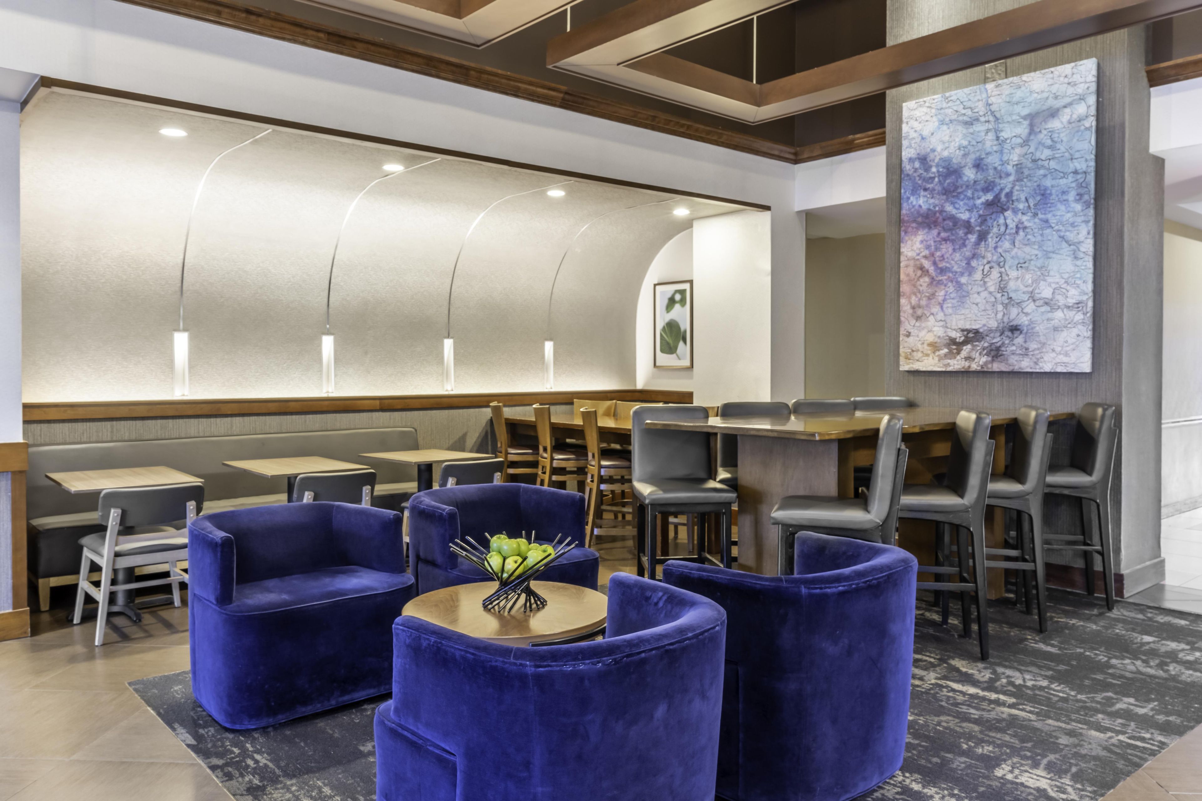Interior moderno de restaurante con sillas de terciopelo azul, una mesa de madera y un cuadro abstracto grande en la pared.