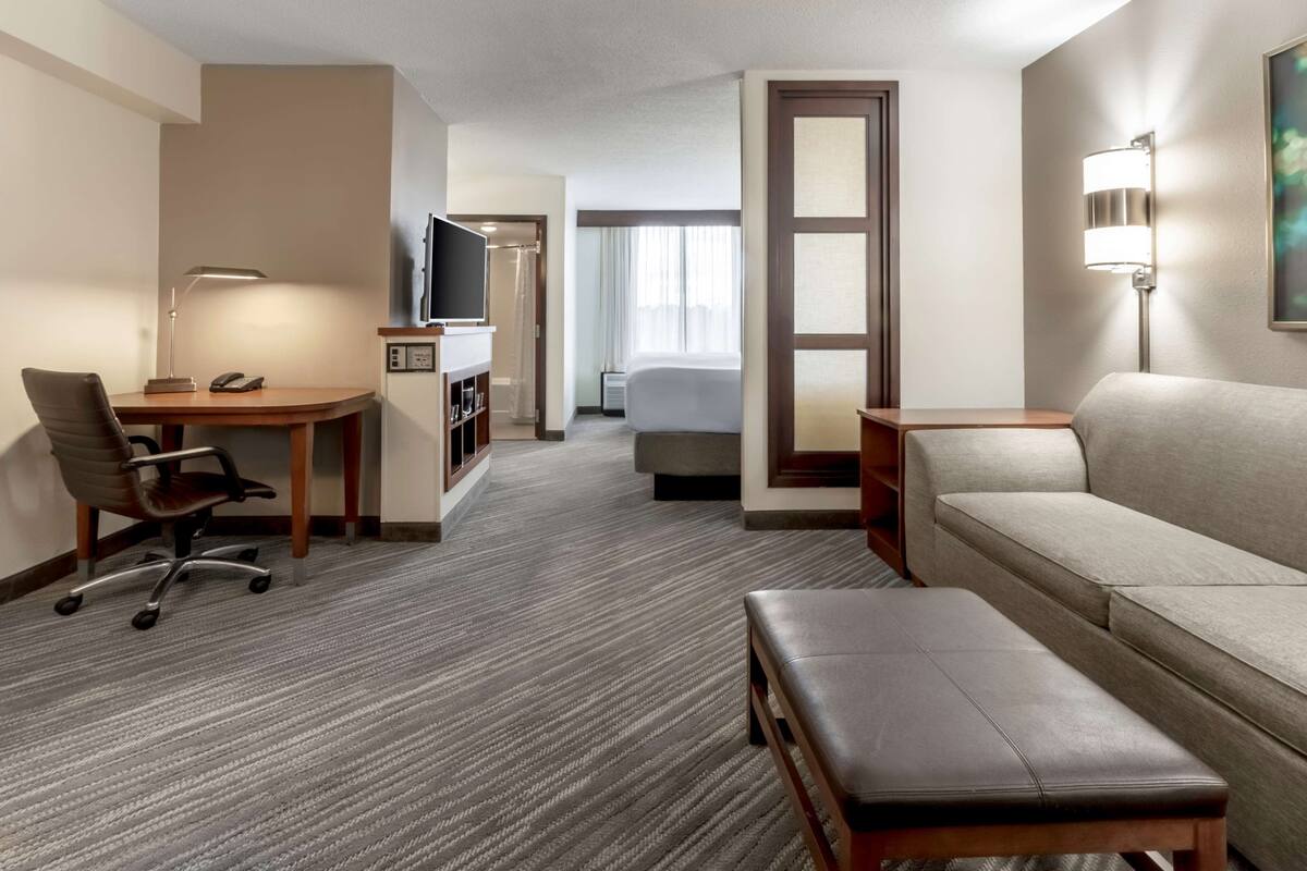 Een hotelkamer met een bureau, stoel, bank en een klein tafeltje. Er is een televisie, een lamp en een bed.