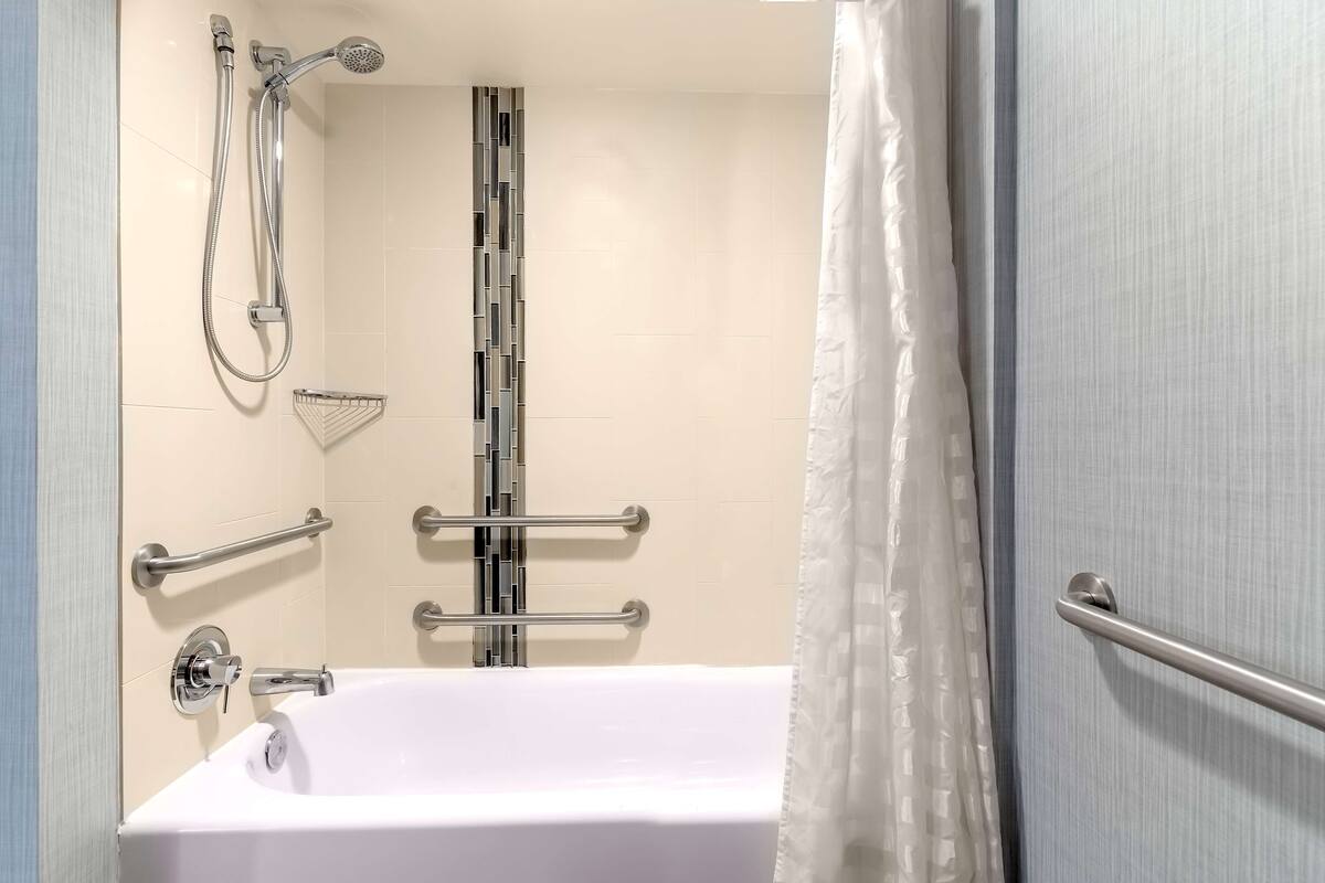 Een moderne badkamer met een witte badkuip, een douche met handdouche en een handgreep.