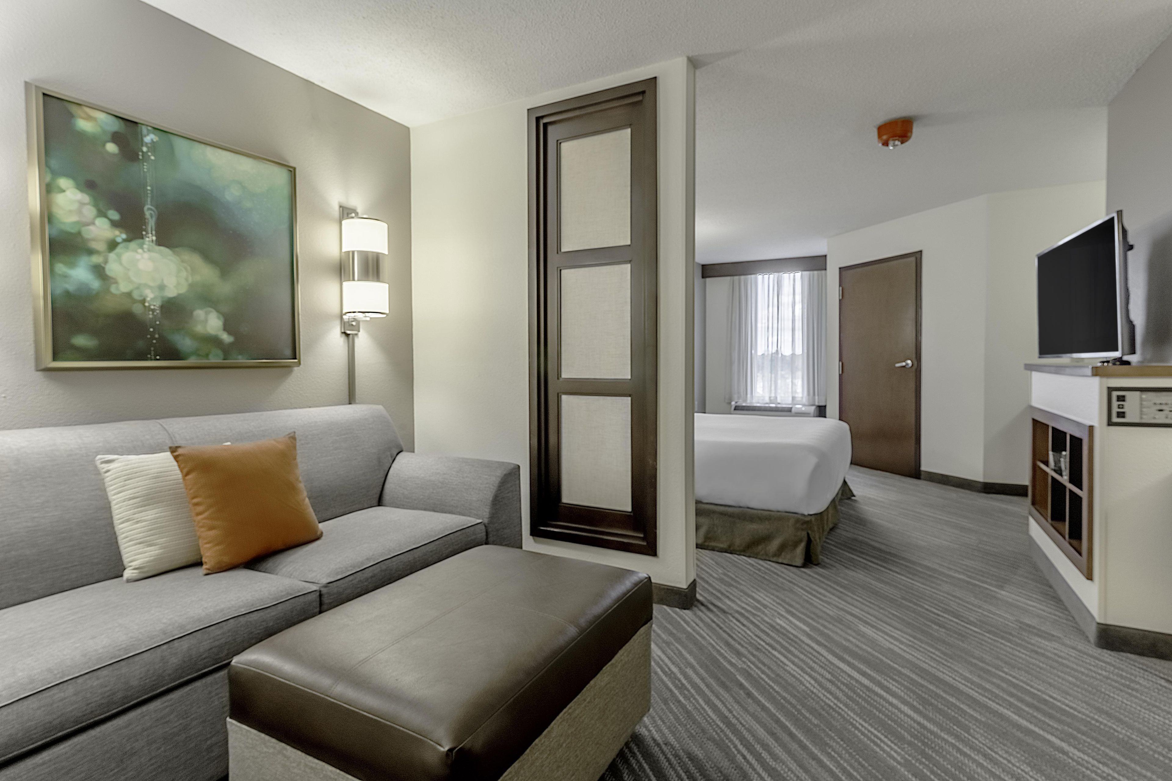 A hotel room with a sofa, a bed, a television, and a painting on the wall.