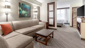 Ein Hotelzimmer mit einer Couch, einem kleinen Tisch, einem Bett, einem Fernseher und einem Bild an der Wand.