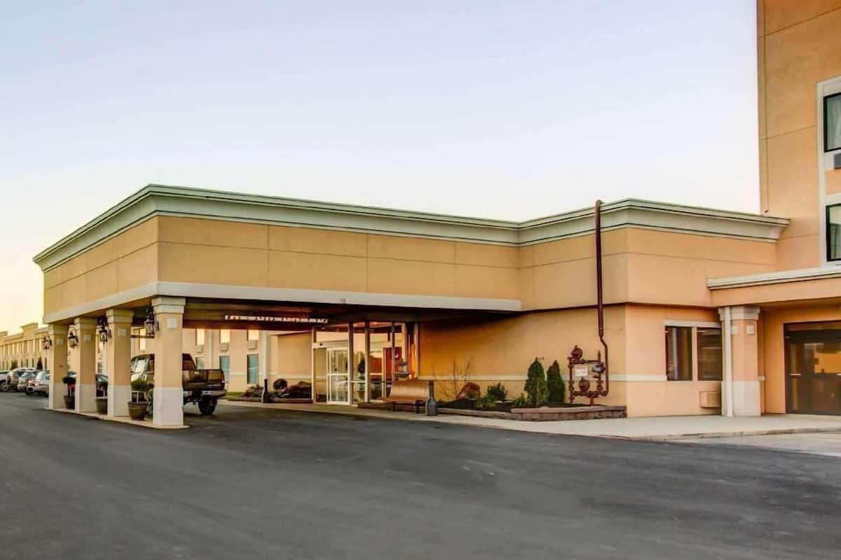 A hotel with a covered outdoor area, a parking lot, and a building with a flat roof.